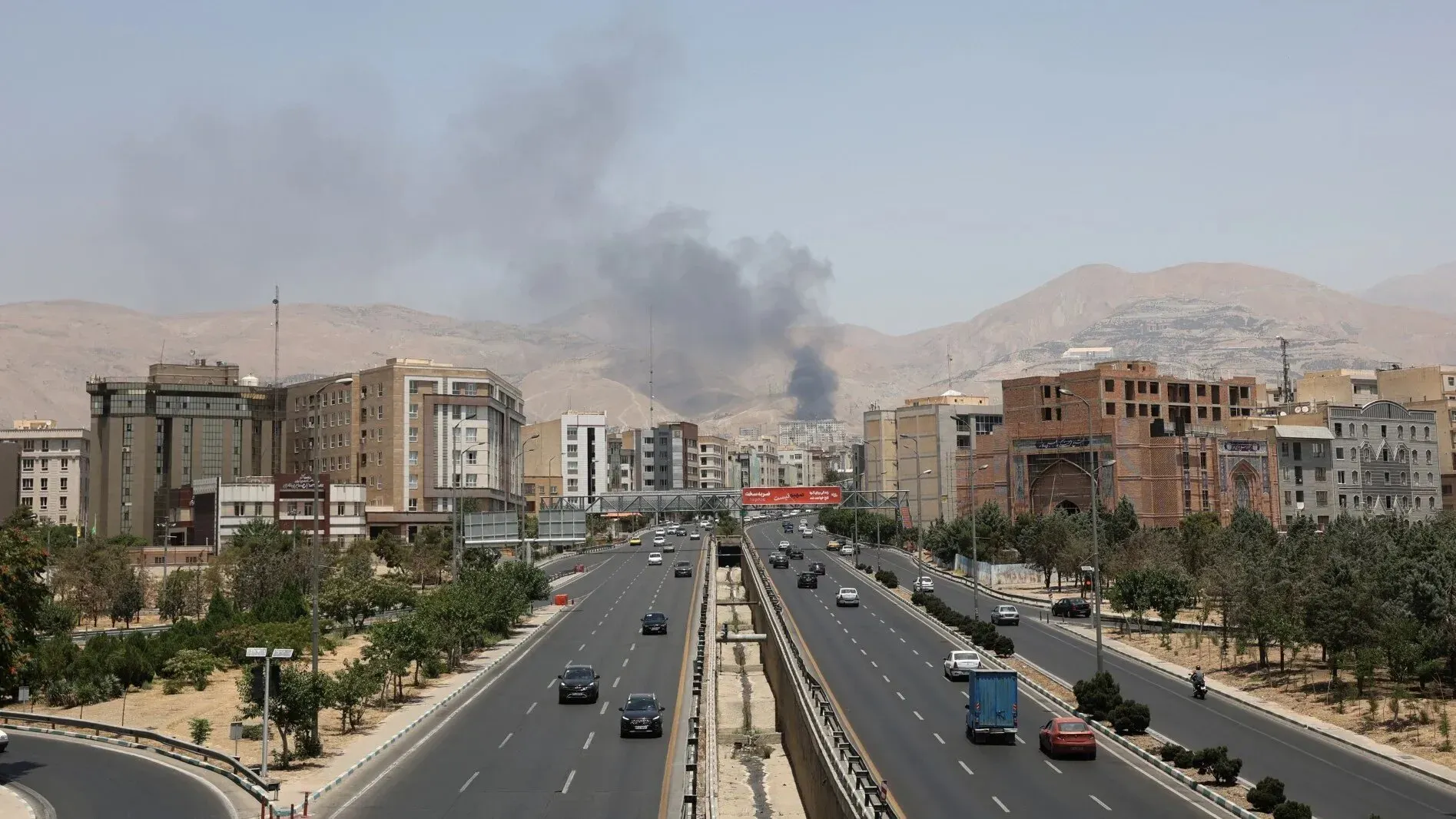 دخان يتصاعد من منطقة سكنية في طهران بعد سقوط صاروخ إسرائيلي، مع وجود سيارات على الطريق وأبنية محيطة.