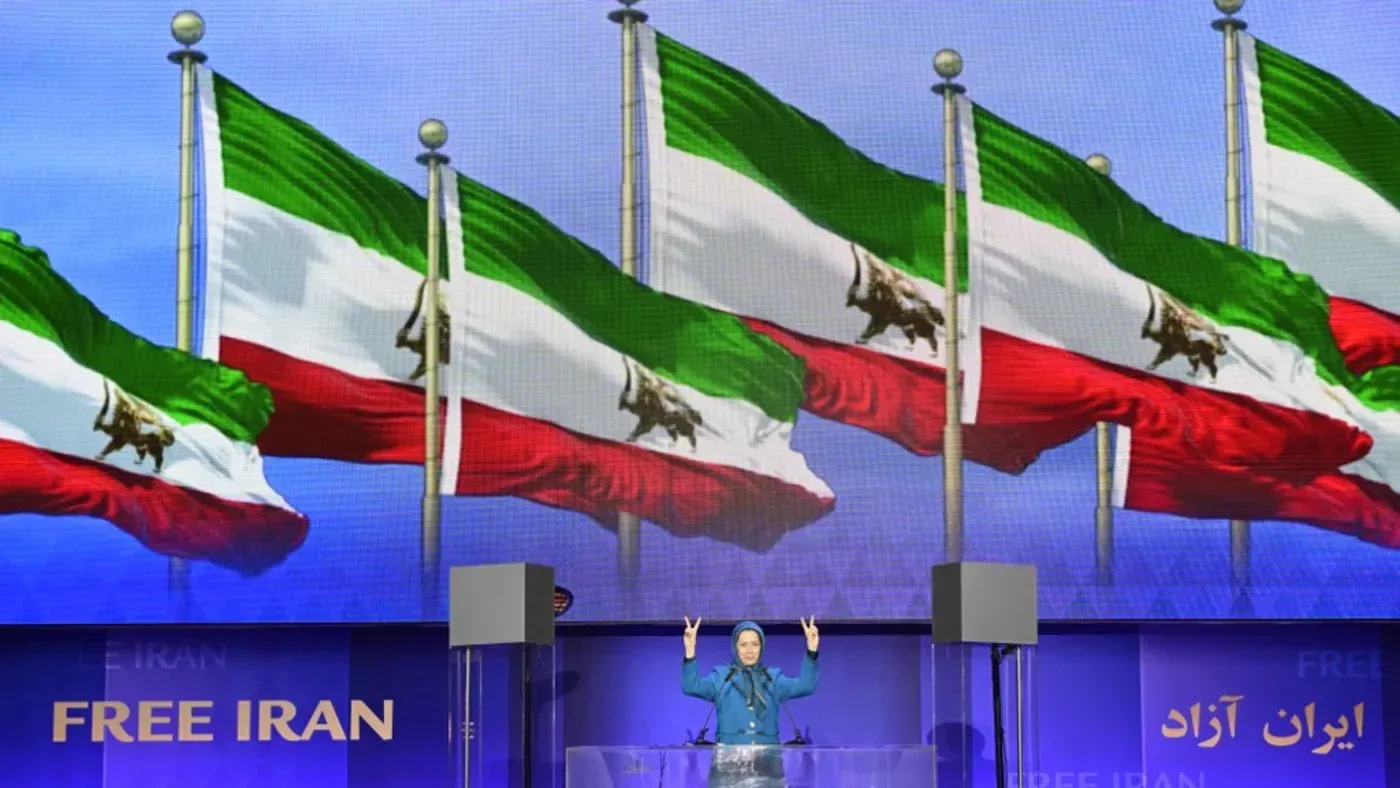 مريم رجوي، زعيمة منظمة مجاهدي خلق، تتحدث أمام أعلام إيران في تجمع لدعم الحكومة المؤقتة المقترحة، في سياق الصراع ضد النظام الإيراني.