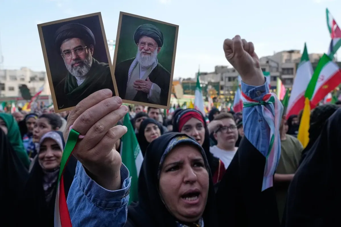 امرأة تحمل صورتين لآية الله خامنئي ورئيسي خلال مظاهرة في إيران، مع وجود حشود من المتظاهرين والأعلام الإيرانية في الخلفية.