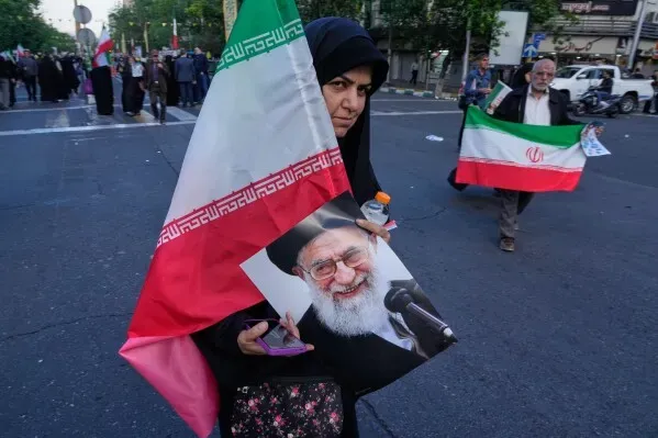 امرأة ترتدي الحجاب وتحمل علم إيران وصورة للمرشد الأعلى آية الله خامنئي خلال تظاهرة في الشارع، تعبيرًا عن الدعم للقدرات النووية والصاروخية.