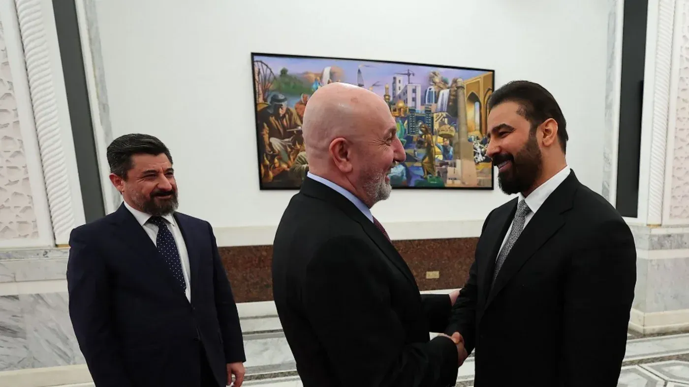 علي الزيدي يتصافح مع الرئيس نزار أميدي، بينما يظهر خلفهما عمل فني، في سياق تكليفه بتشكيل الحكومة العراقية الجديدة.