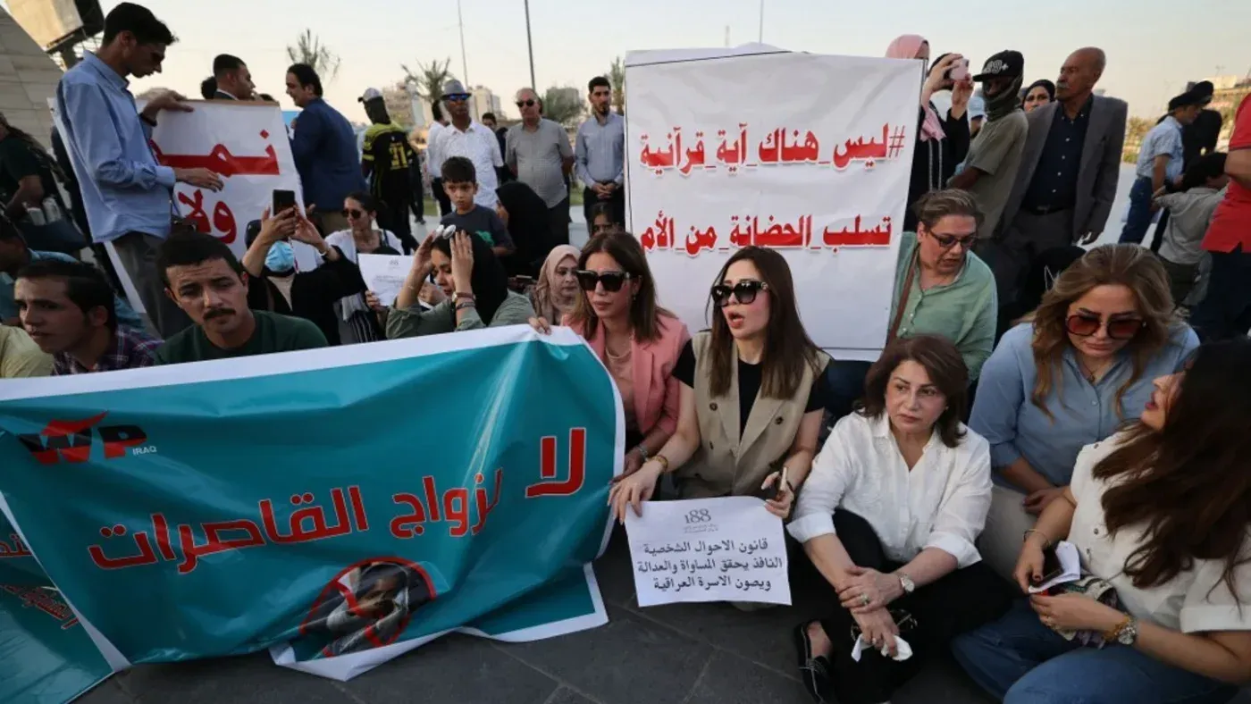 محتجون في العراق يجلسون خلال مظاهرة ضد قانون زواج الأطفال، يحملون لافتات تعبر عن رفضهم للتعديلات المقترحة.