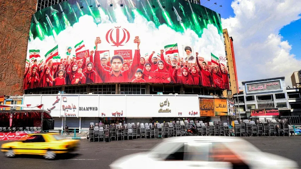 جدارية ضخمة في طهران تظهر مجموعة من الأشخاص يرتدون ملابس حمراء، يرفعون الأعلام الإيرانية ويعبرون عن التضامن الوطني وسط أجواء احتفالية.
