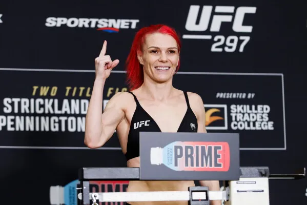 مقاتلة UFC ماكنزي ديرن ترفع إصبعها وتبتسم خلال مراسم الوزن قبل دفاعها عن لقب فئة القش في بطولة UFC 297.