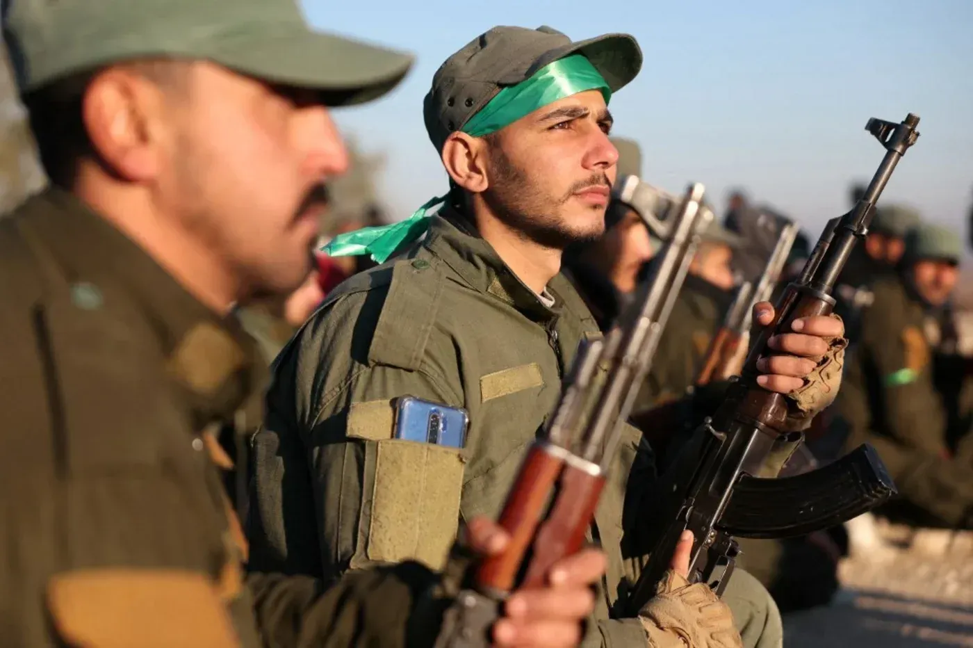 مقاتلون يحملون أسلحة في تجمع عسكري، يرتدون زيًا موحدًا، يعكس استعدادهم لمواجهة تهديدات تنظيم الدولة الإسلامية في سوريا.