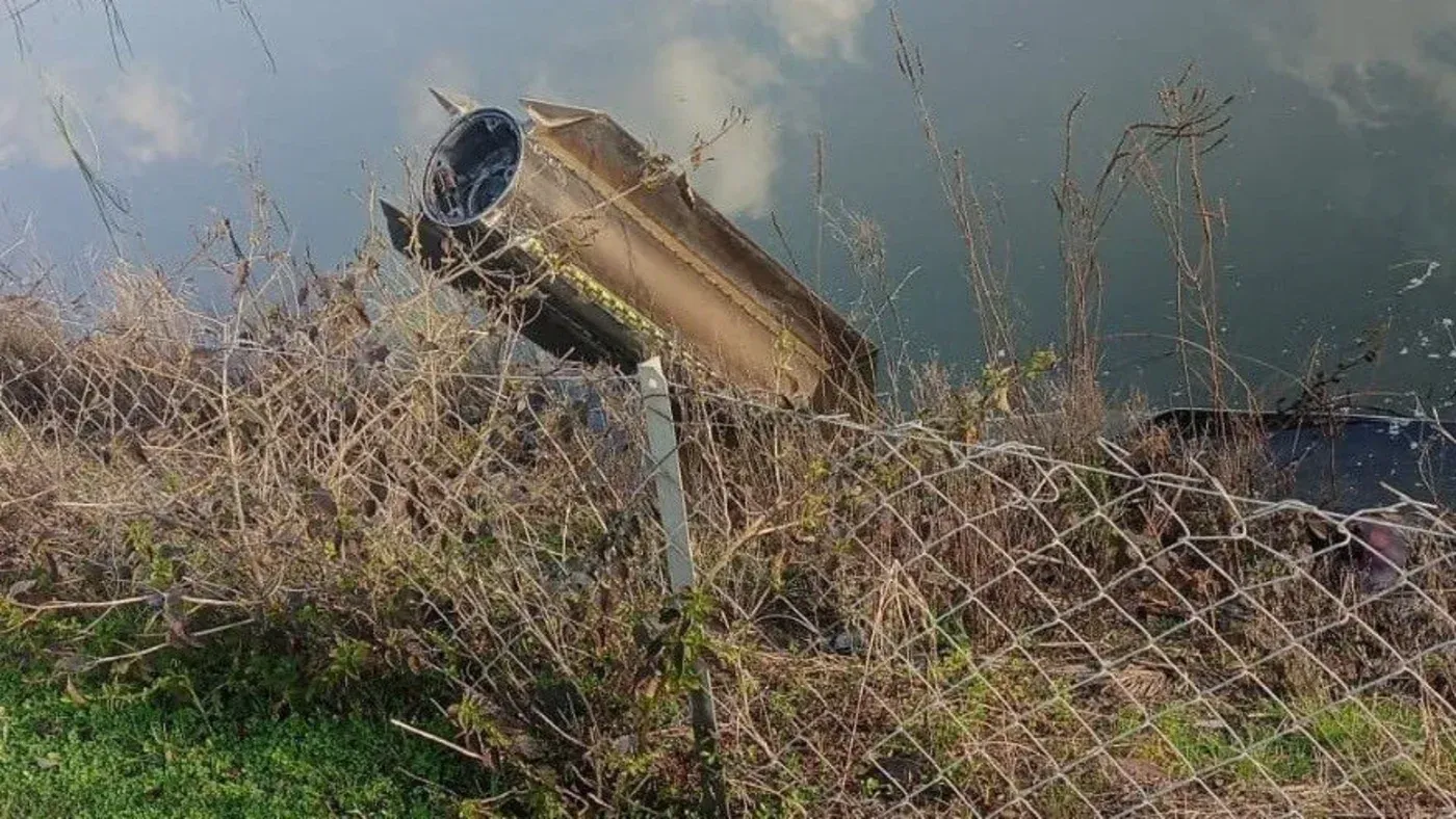 صاروخ باليستي معطل بالقرب من مجرى مائي، محاط بنباتات جافة وسياج، يشير إلى حادثة اعتراض صاروخ إيراني قرب تركيا.