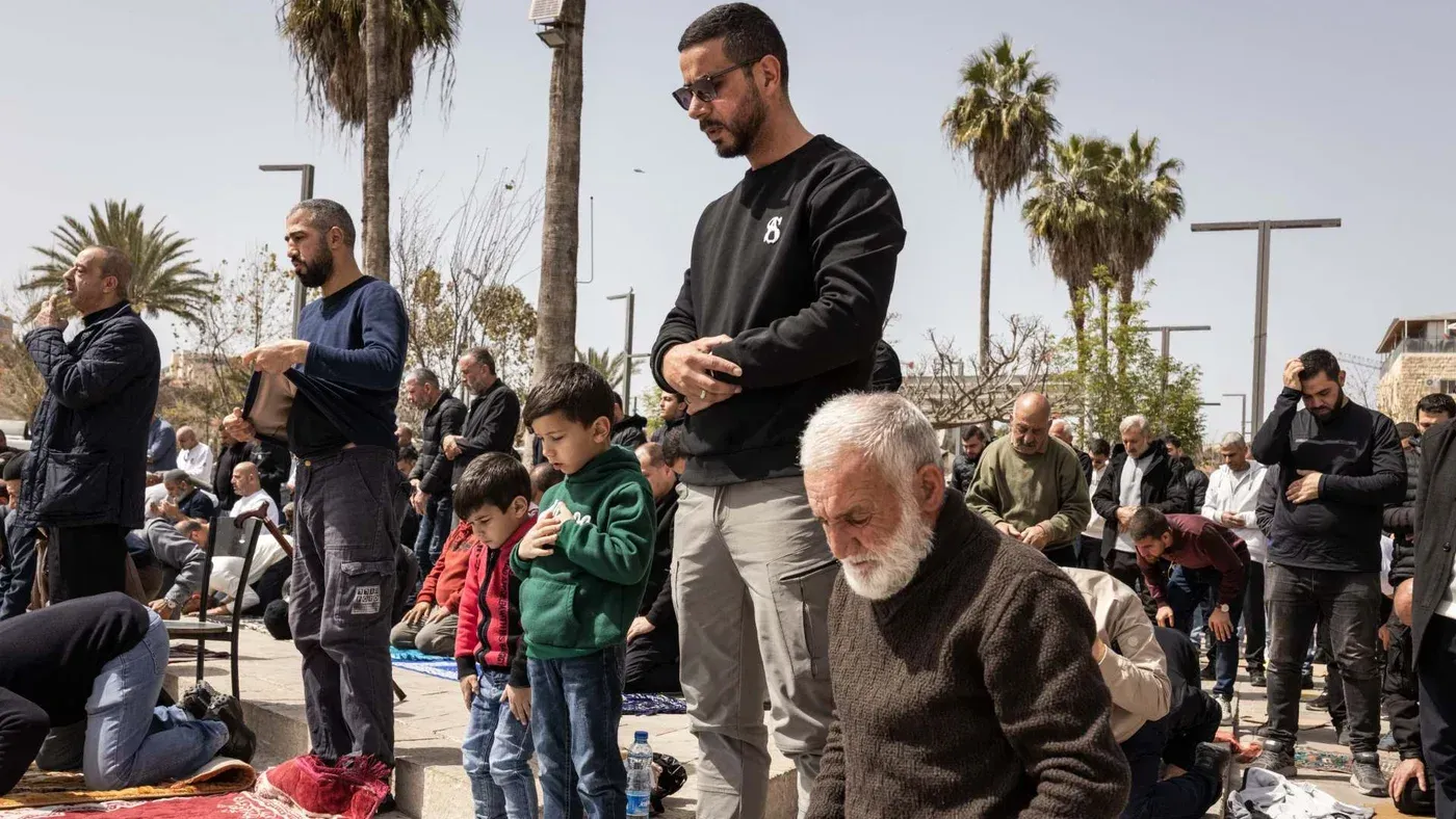 مجموعة من الفلسطينيين يؤدون الصلاة في الهواء الطلق، مع وجود أطفال ورجال ونساء، في سياق تزايد الاضطهاد الديني خلال رمضان.