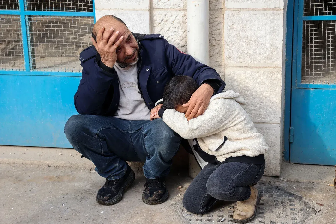 رجل وطفل يجلسان على الأرض، يعبران عن الحزن والقلق، في سياق توتر الأوضاع في الضفة الغربية وتأثيرها على المجتمعات.