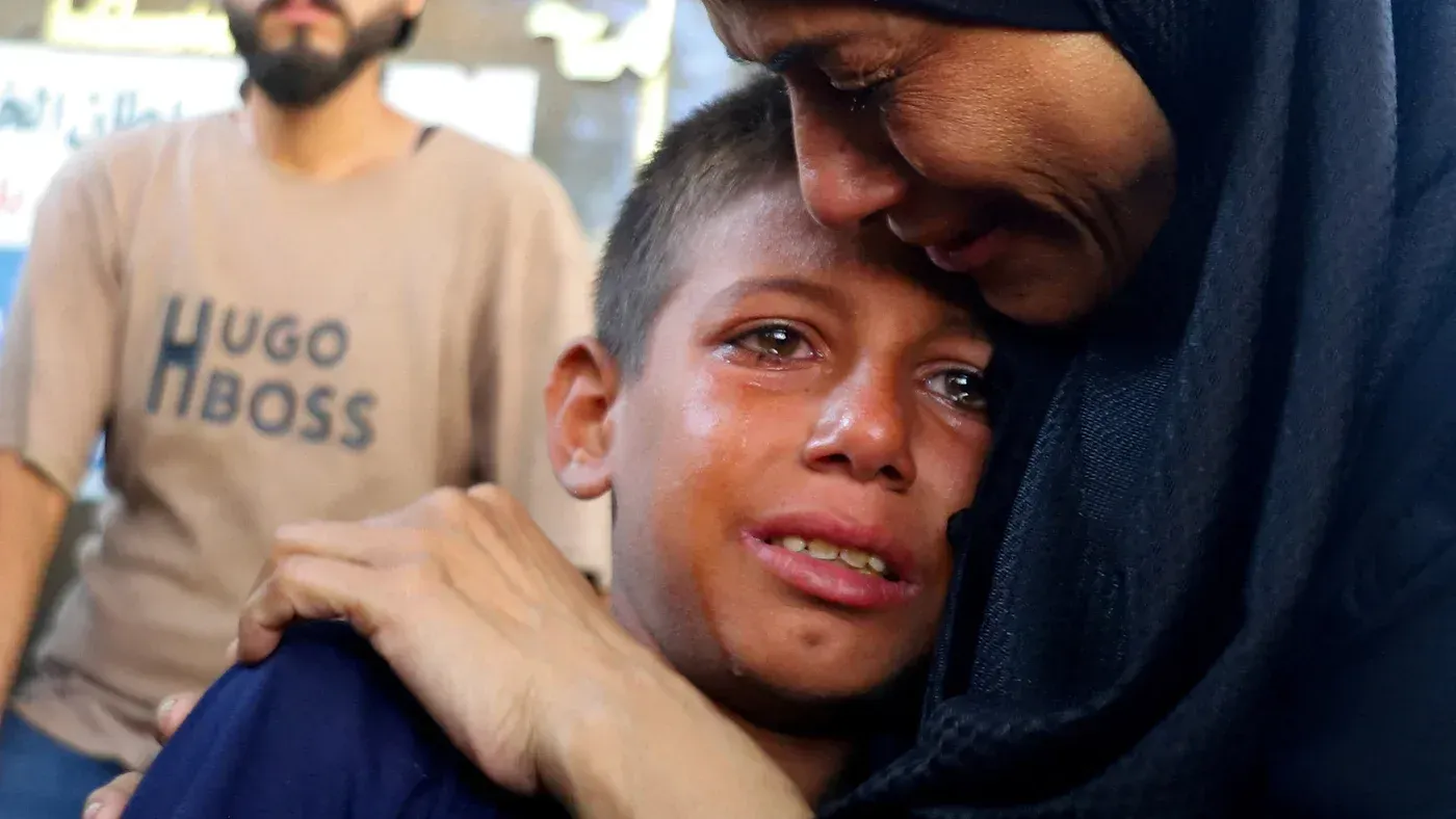 امرأة تعانق طفلاً يبكي في غزة، تعبيراً عن الحزن والألم بسبب الأحداث الجارية. تعكس الصورة معاناة المدنيين خلال الصراع.