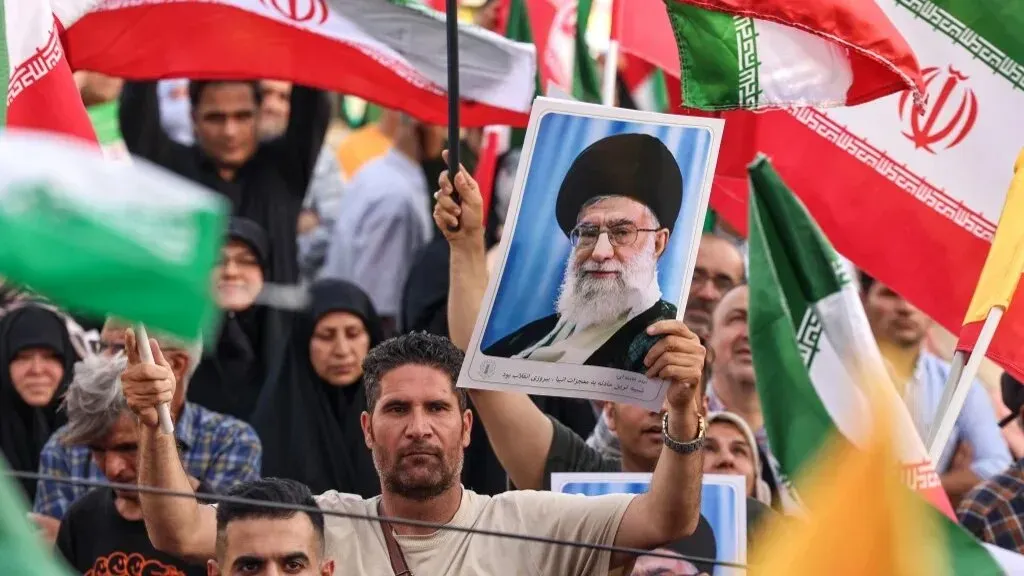 محتجون إيرانيون يحملون أعلام إيران وصورة للمرشد الأعلى علي خامنئي، يعبرون عن دعمهم في سياق التطورات السياسية الأخيرة.