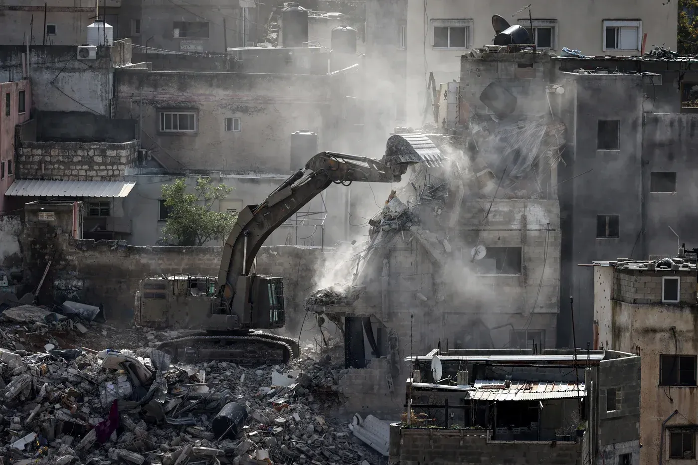 جرافة تهدم مبنى في مخيم نور شمس للاجئين، محاطة بأنقاض المباني المدمرة، مما يعكس آثار عمليات الهدم الواسعة في الضفة الغربية.