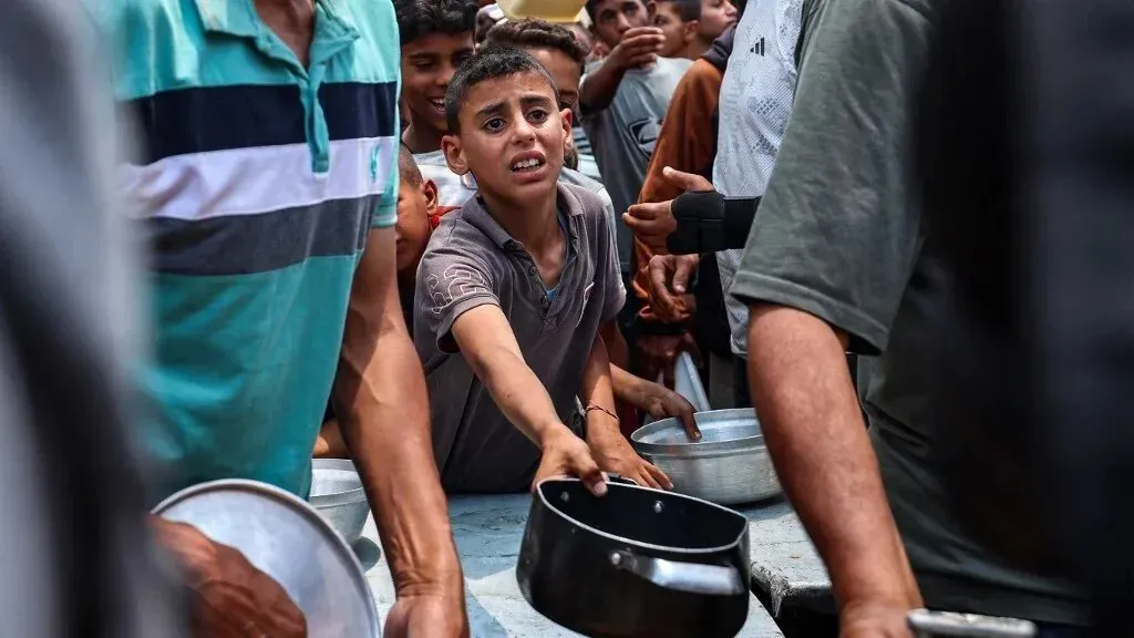 طفل فلسطيني يظهر في حالة من القلق أثناء محاولته الحصول على الطعام وسط حشد من الناس في غزة، في ظل أزمة إنسانية متفاقمة.