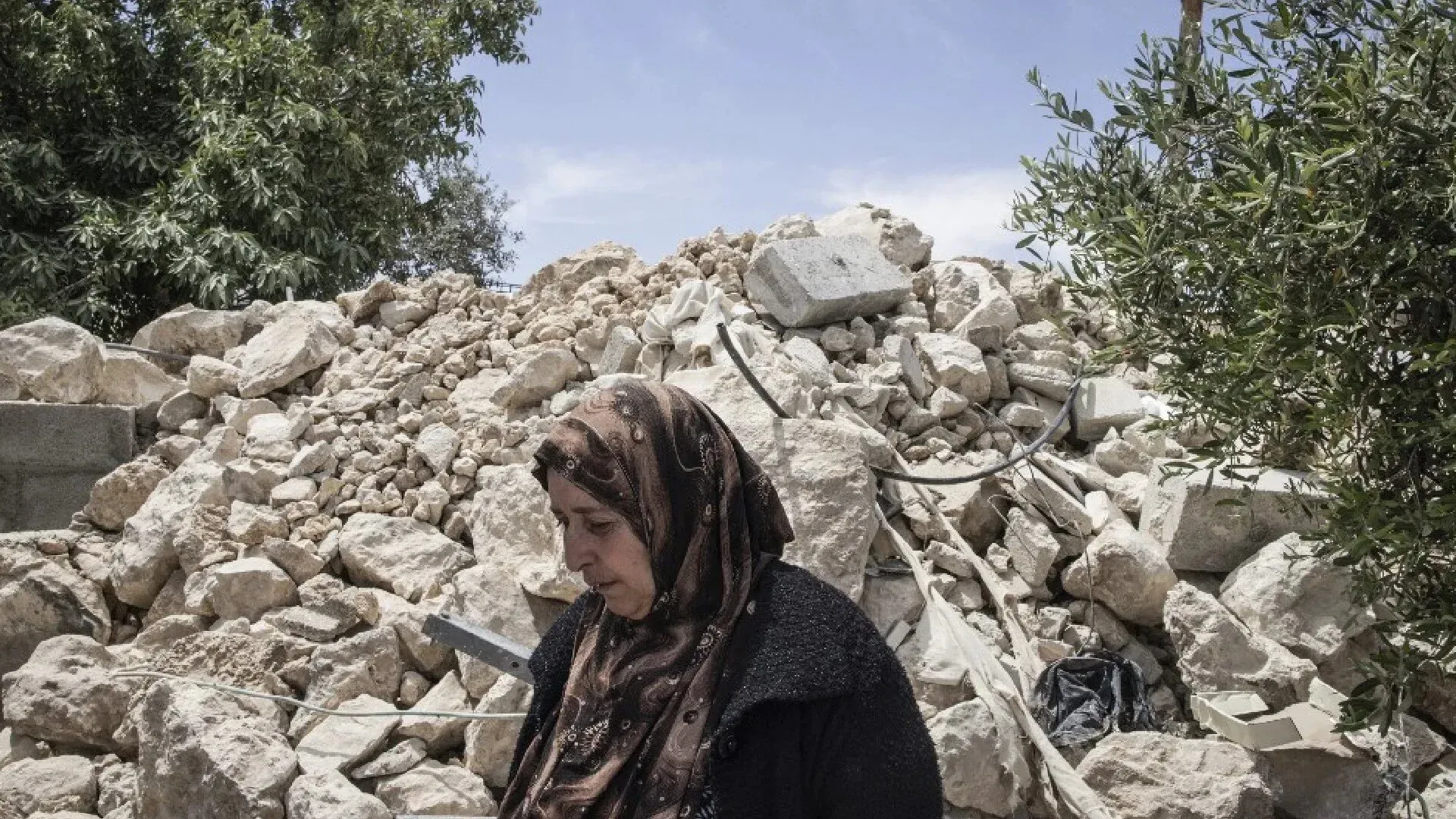 امرأة فلسطينية واقفة أمام أنقاض منزل مهدوم، تعكس معاناتها جراء العنف المستمر من المستوطنين في مسافر يطا.