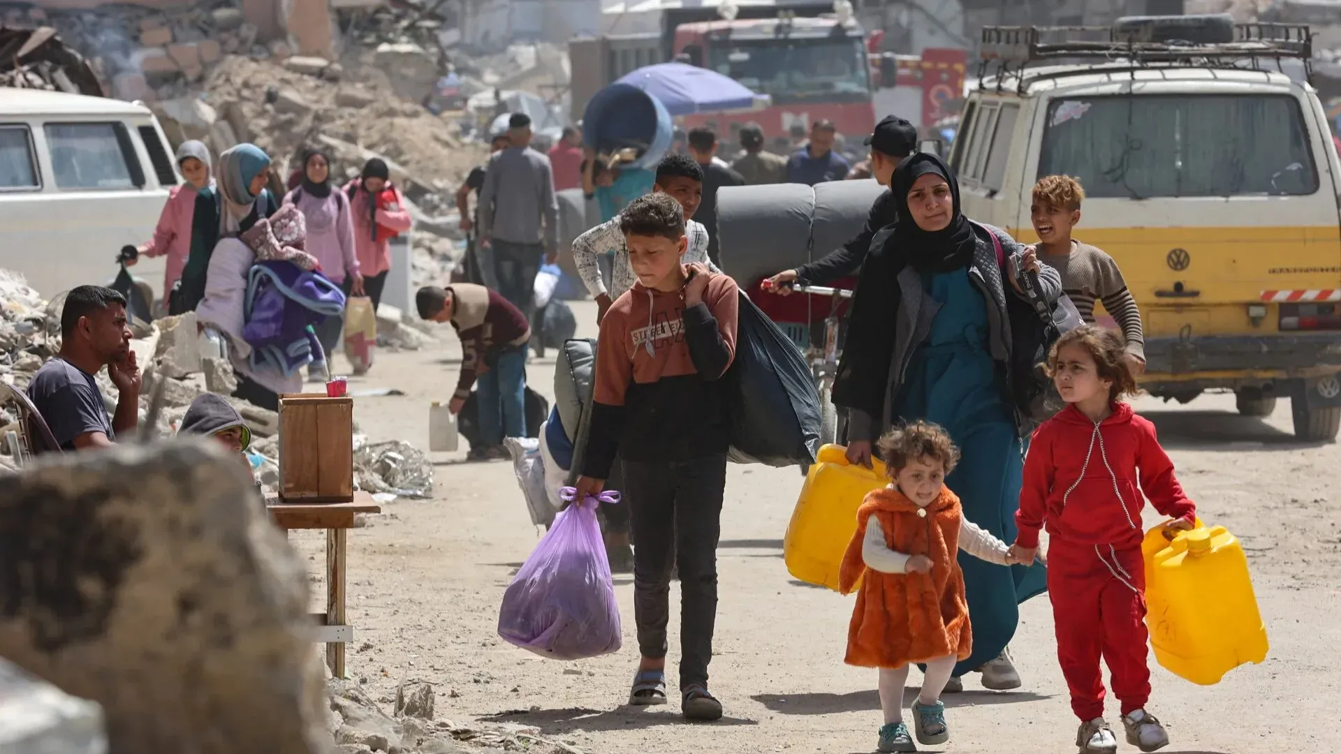 عائلات فلسطينية تحمل الأمتعة والأغراض في منطقة مدمرة، تعبيرًا عن معاناتهم في ظل الظروف الصعبة في غزة.
