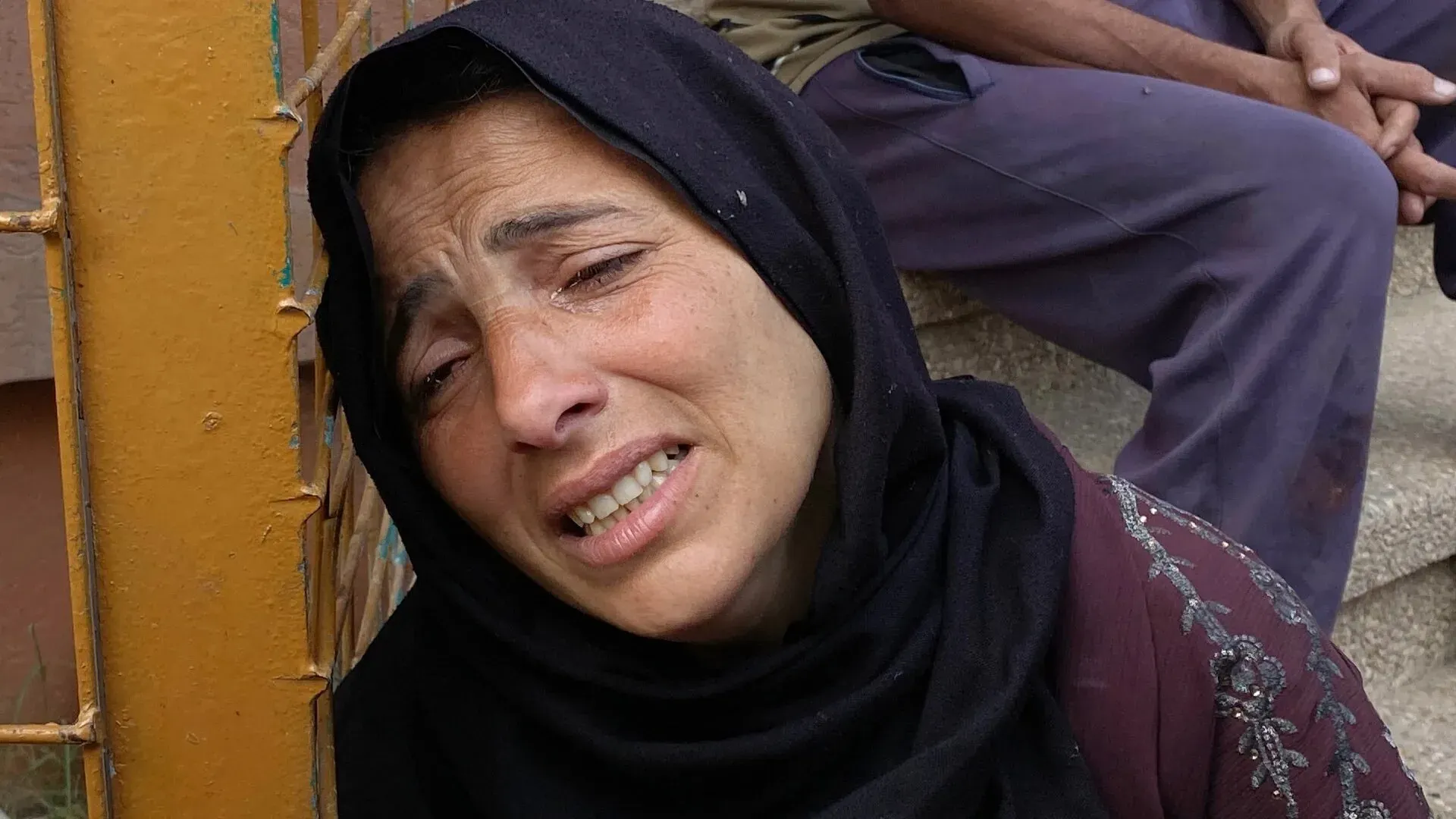 امرأة تبكي بحرقة، تعبر عن الحزن العميق لفقدان منزلها في غزة، بينما يظهر شخص آخر يجلس بجوارها في الخلفية.