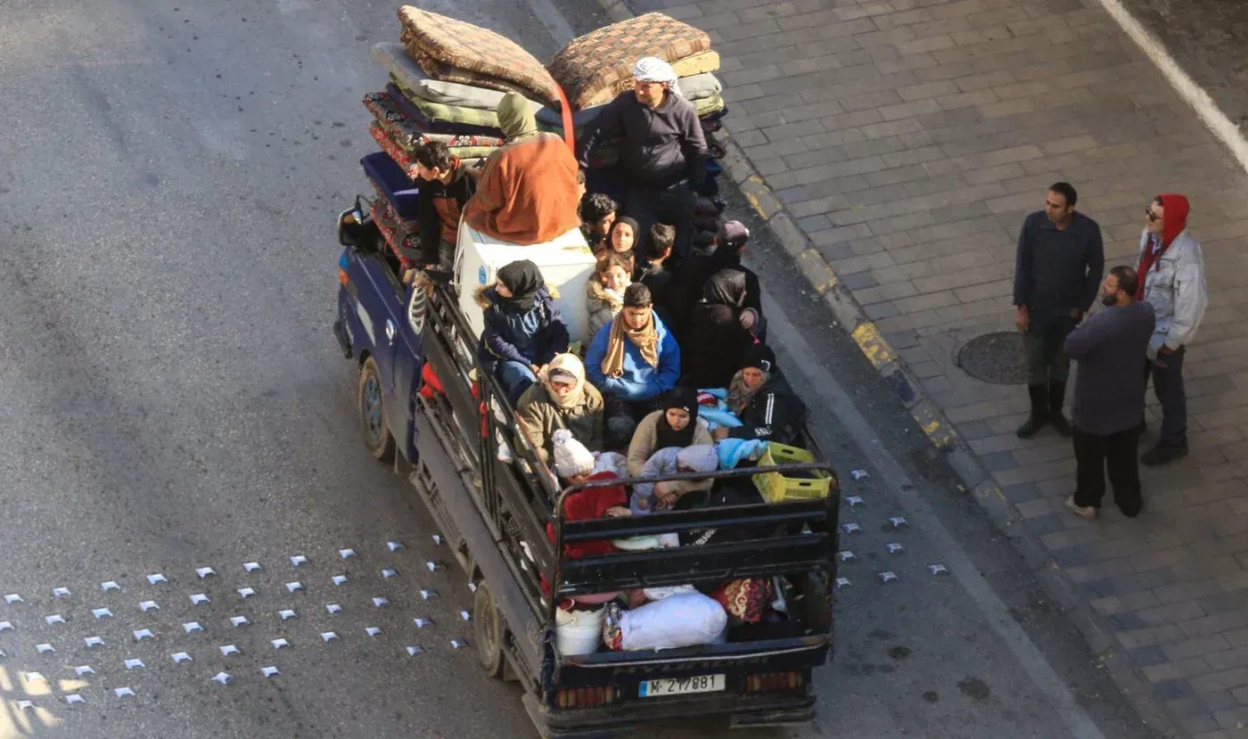 عائلات لبنانية نازحة تجلس في شاحنة محملة بالممتلكات، بينما تتجه نحو مناطق أكثر أمانًا بسبب الغارات الإسرائيلية.