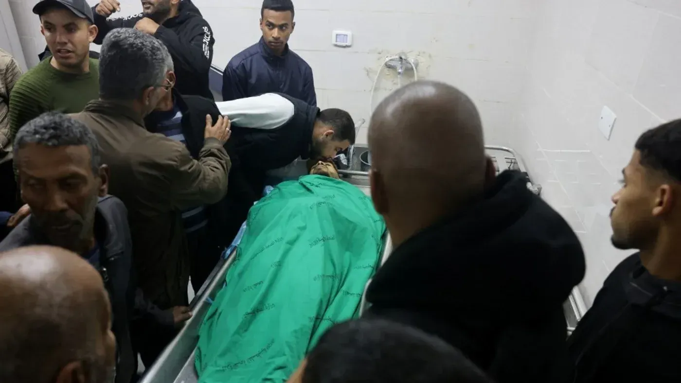 تجمع حشد من الناس حول جثمان فلسطيني في مستشفى بغزة، حيث يظهر الحزن والقلق في وجوههم بعد الهجمات الإسرائيلية الأخيرة.