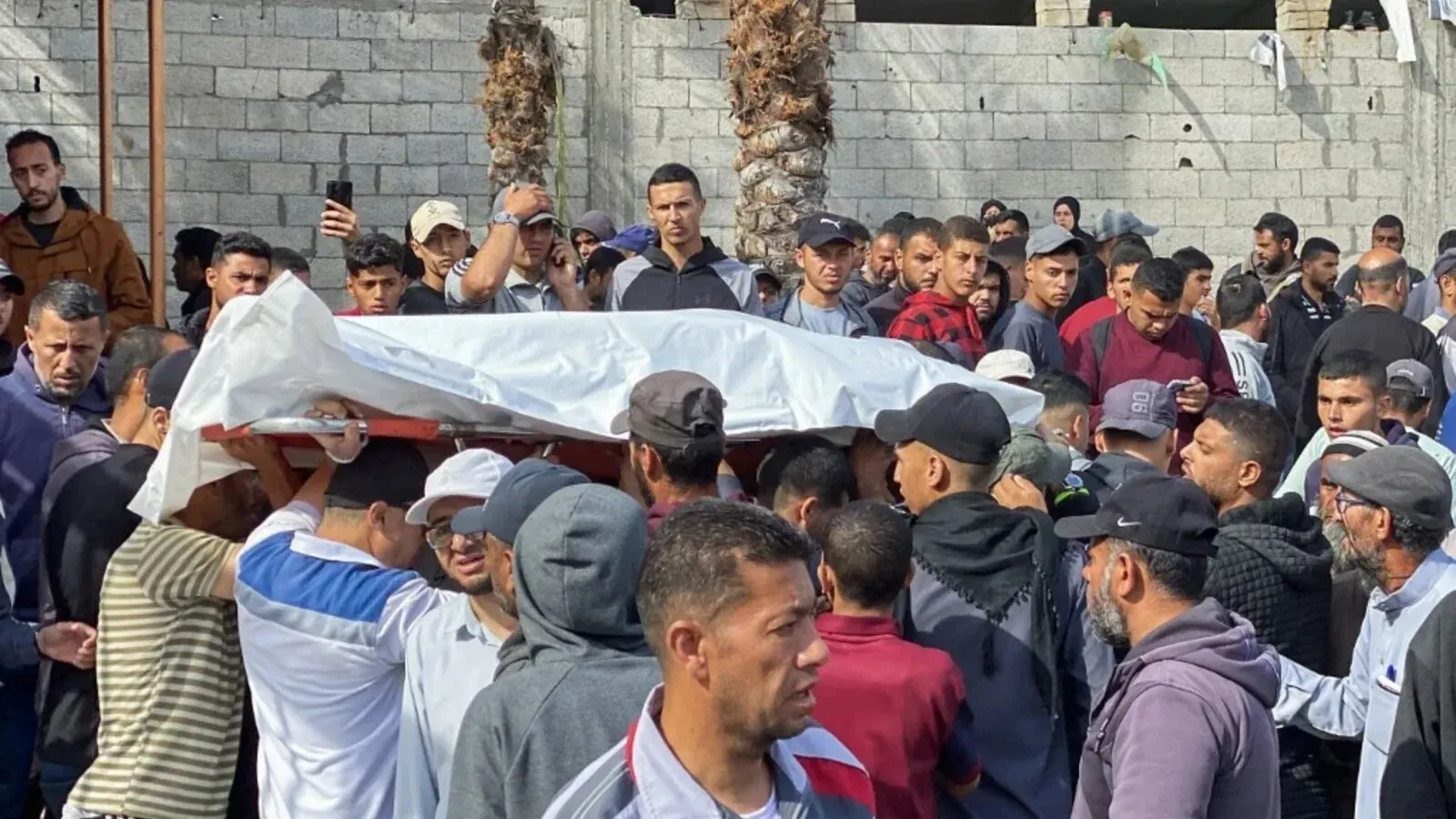 تجمع حشد من الرجال حول نعش مغطى في غزة، حيث يشارك الجميع في مراسم تشييع ضحايا الغارات الجوية الإسرائيلية الأخيرة.