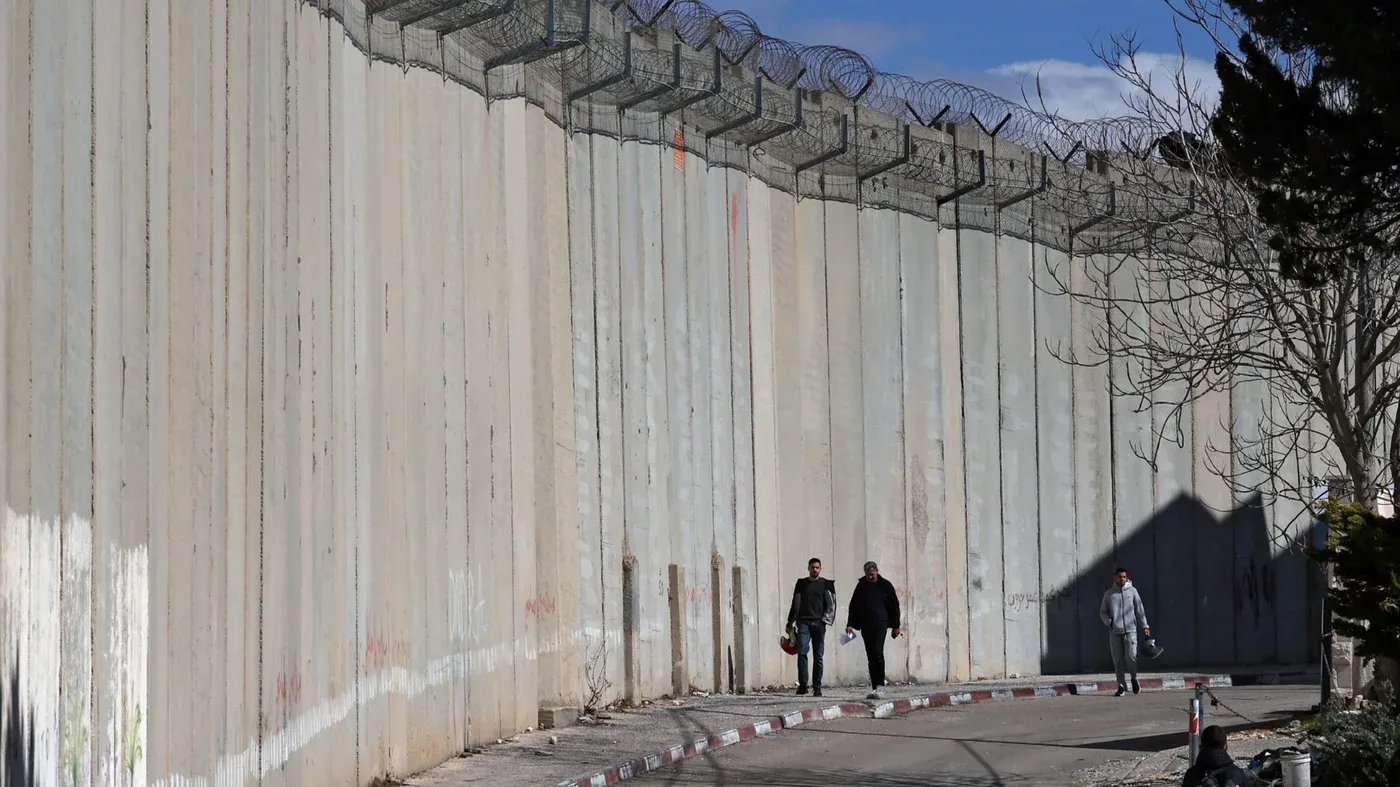 عمال فلسطينيون يسيرون قرب جدار الفصل في الضفة الغربية، حيث يحاولون عبور الجدار بحثاً عن عمل في القدس، وسط توترات متزايدة.