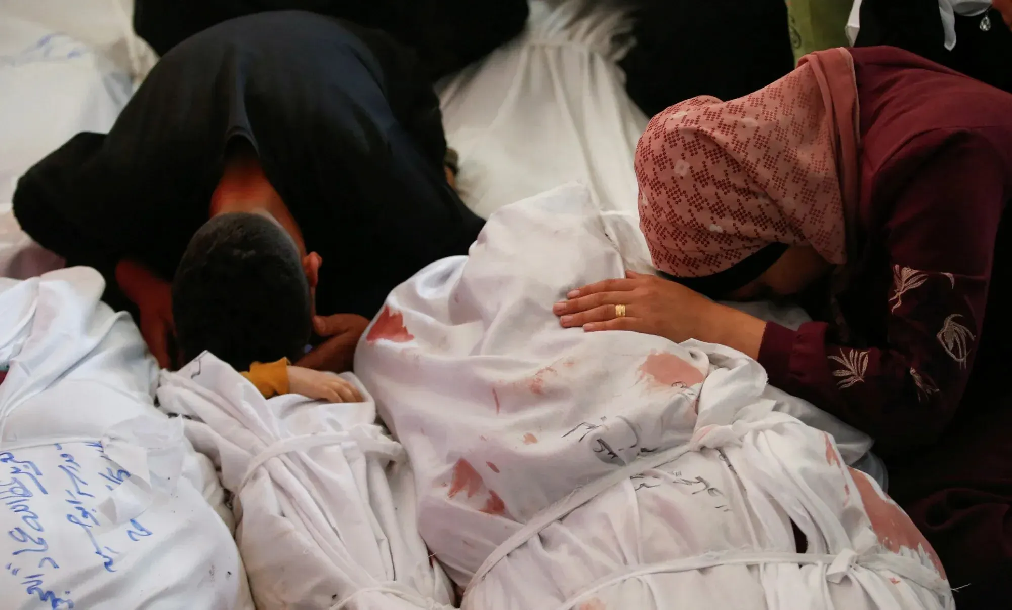 مشهد مؤلم لعائلات فلسطينية تبكي فوق جثث مغطاة بالأكفان، تعبيرًا عن الحزن بعد الغارات الجوية الإسرائيلية في غزة.
