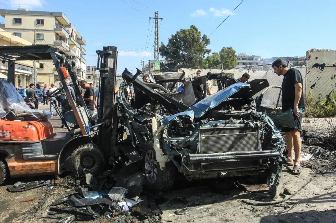 موقع حادث الهجوم الإسرائيلي في كفر رمان، يظهر سيارة مدمرة وسط تجمعات من الناس، مما يعكس تصعيد العنف في لبنان.