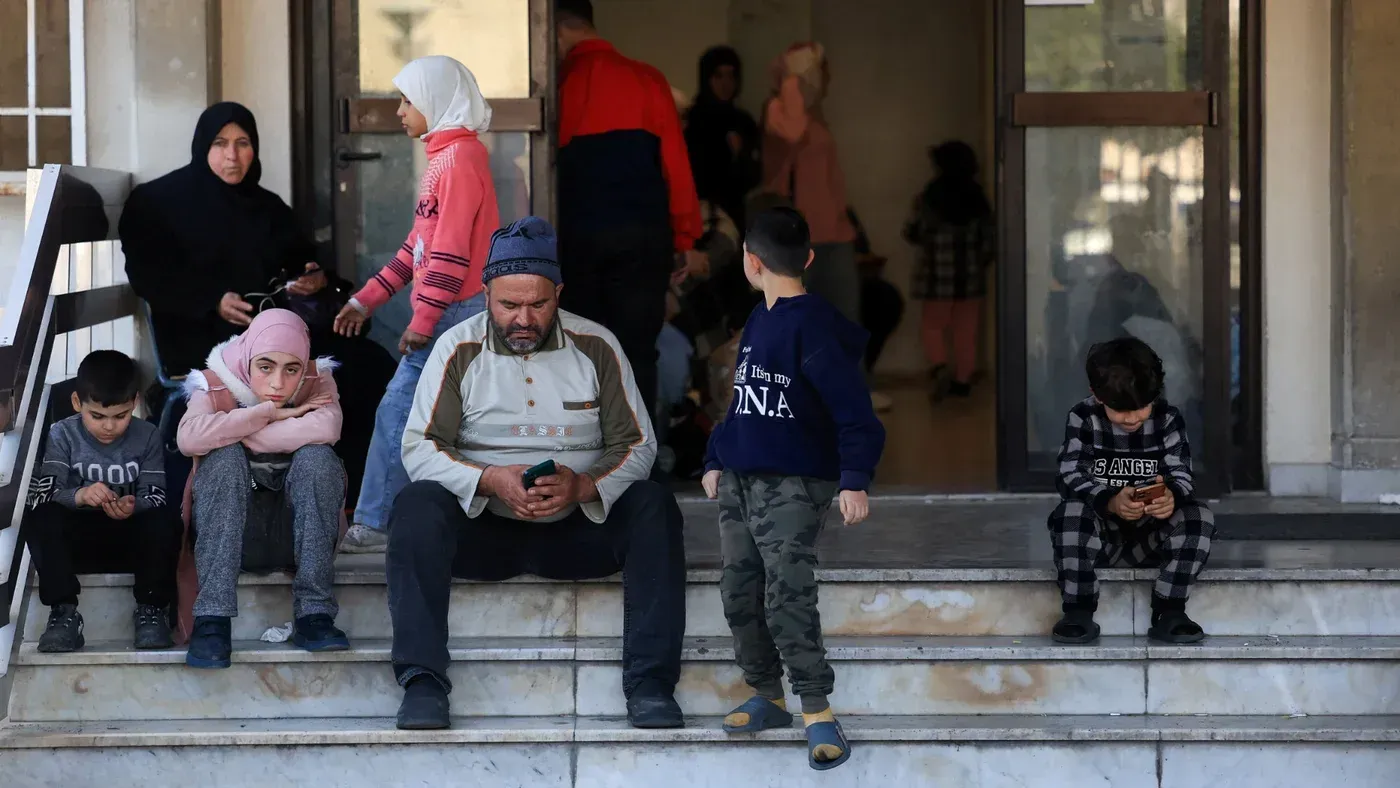 عائلات نازحة تجلس على درجات مبنى، تعبيرات القلق واضحة على وجوههم، في ظل التصعيد العسكري في جنوب لبنان.