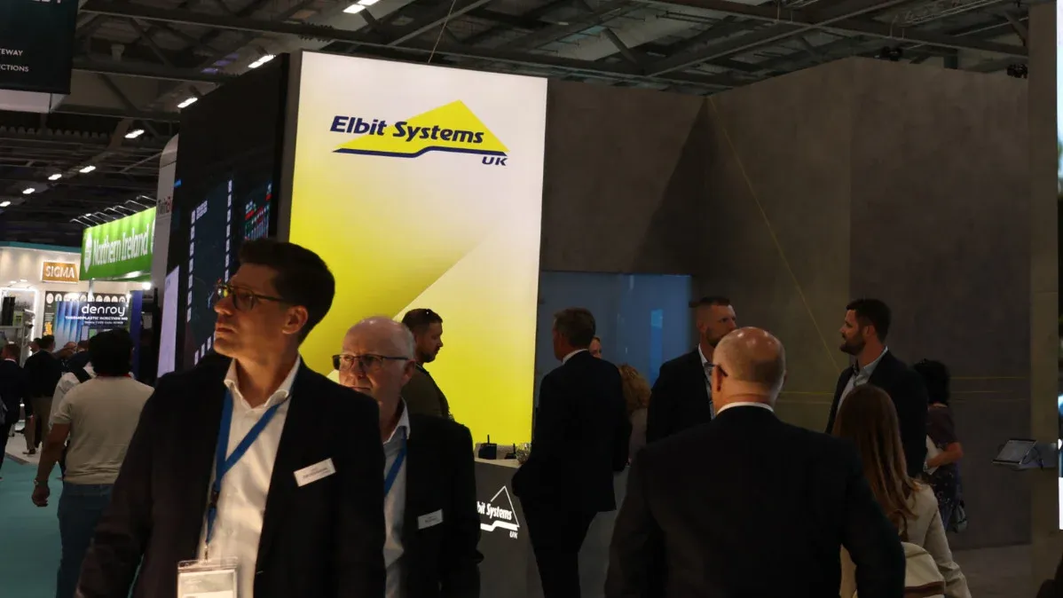 وفد زوار في معرض دفاعي أمام شعار شركة Elbit Systems الإسرائيلية المتخصصة في الطائرات المسيّرة وأنظمة المراقبة.