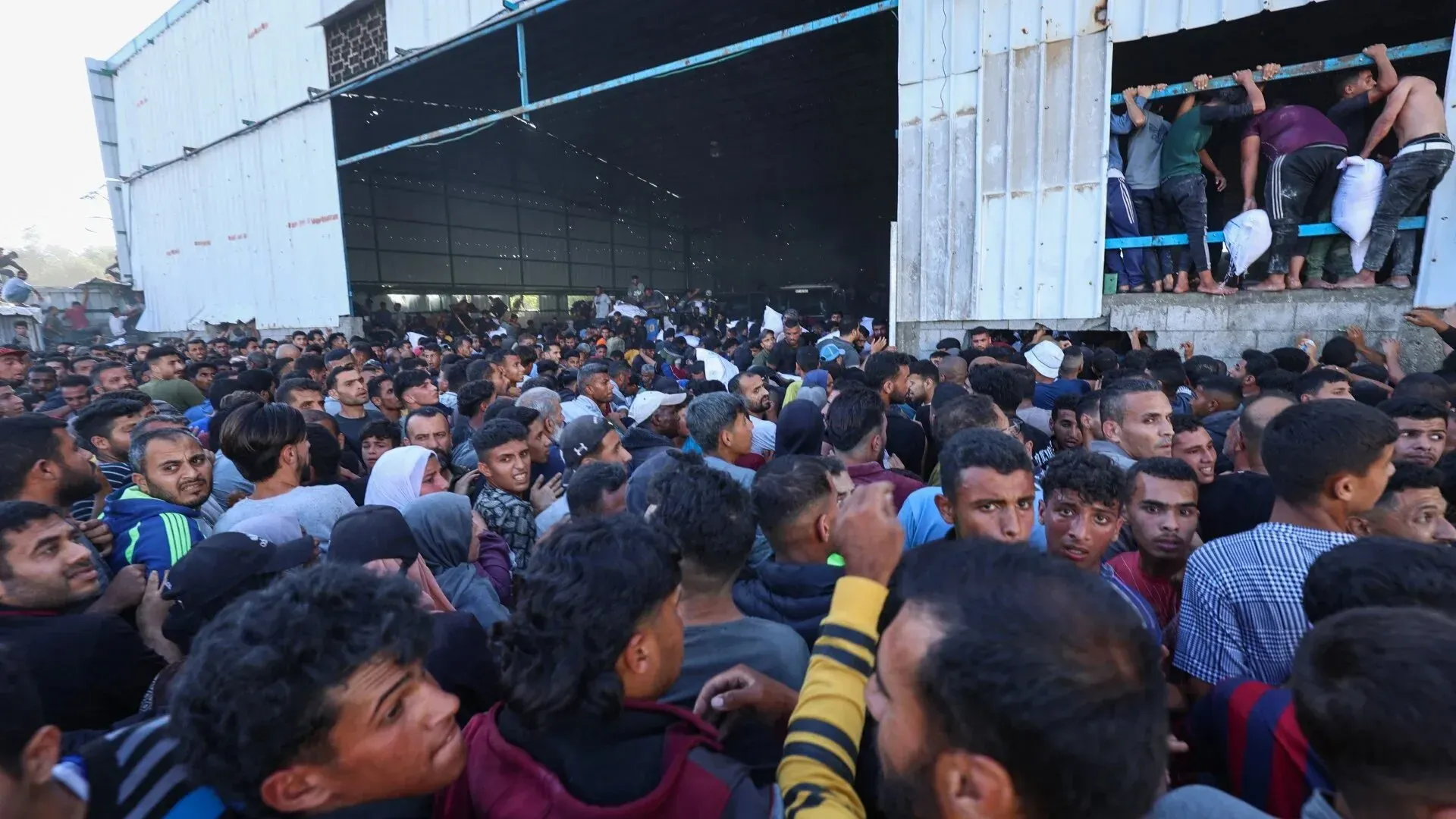 حشود كبيرة من الفلسطينيين تتجمع أمام مستودع في غزة، بحثًا عن المساعدات الإنسانية وسط الظروف الصعبة والتهجير المحتمل.