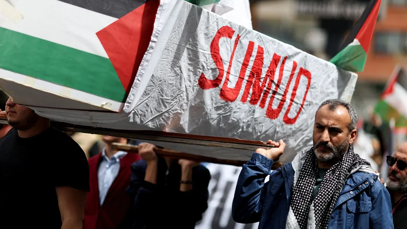 محتجون يحملون نعشًا مكتوبًا عليه "صمود" خلال مظاهرة تضامن مع غزة، مع أعلام فلسطينية ترفرف في الخلفية.