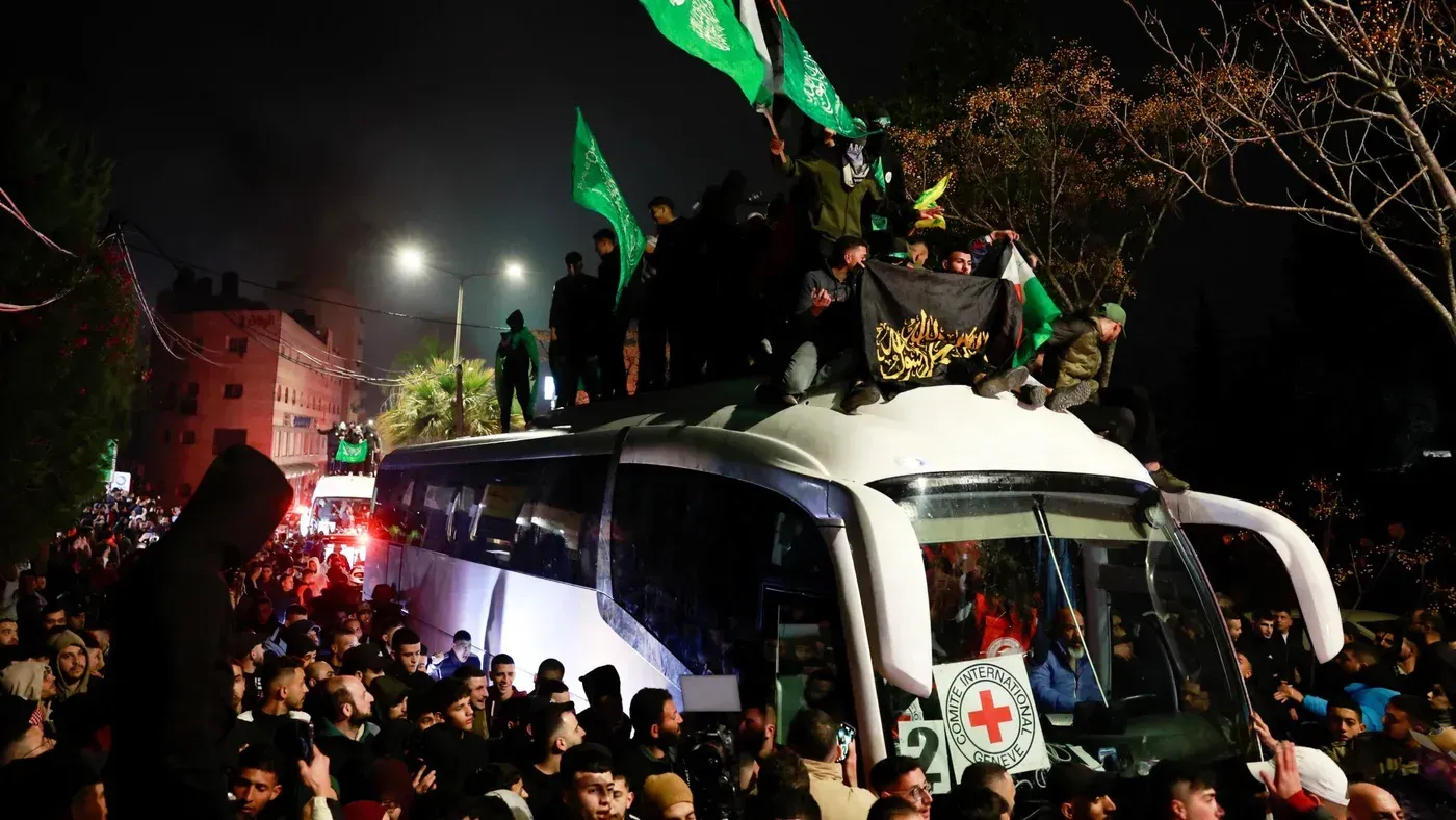 حشود من الناس يحتشدون حول حافلة تحمل أسرى فلسطينيين محررين، مع أعلام حماس ترفرف في سماء الليل.
