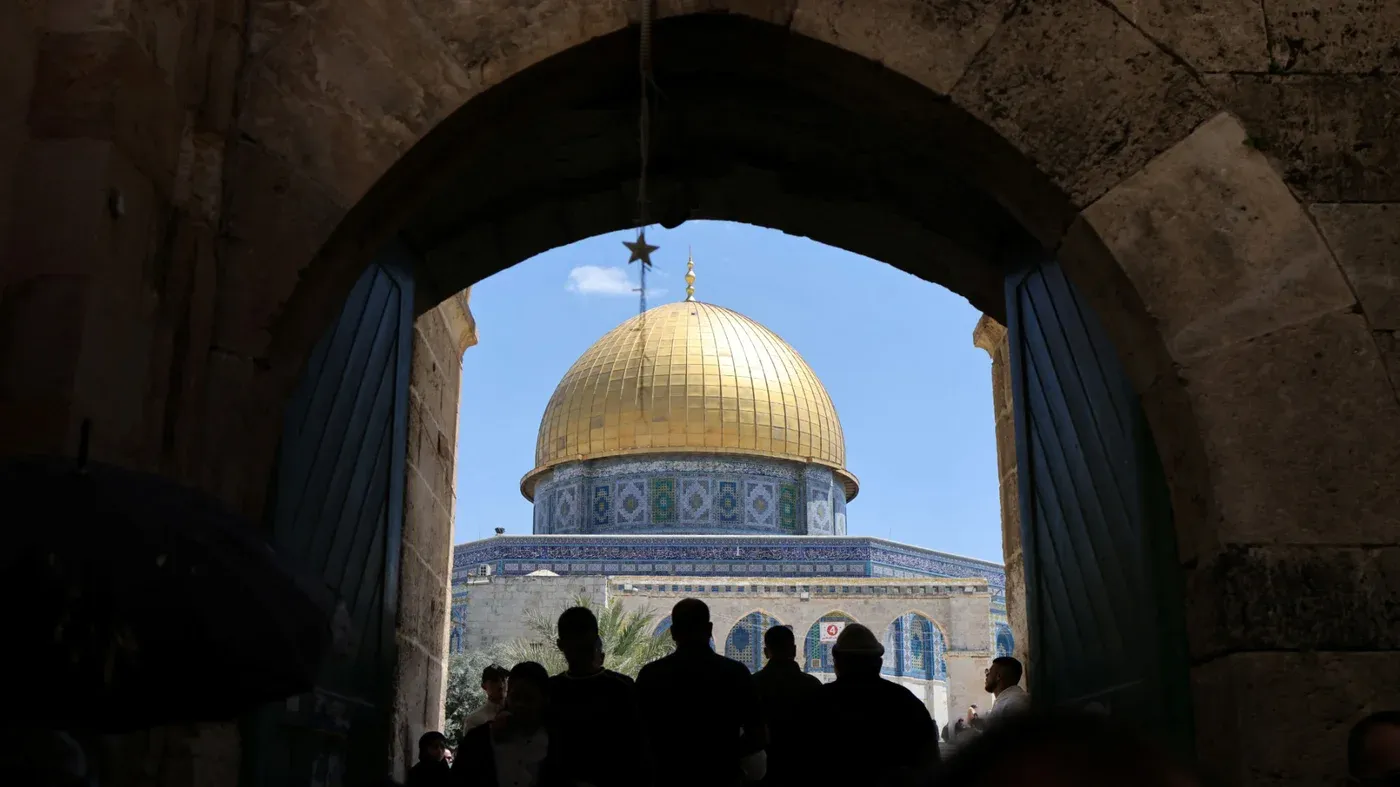 من خلال بوابة تاريخية، يظهر المسجد الأقصى بأقمار ذهبية، بينما يتجمع عدد من الزوار في الداخل، مما يعكس التوترات حول السيطرة الإسرائيلية.