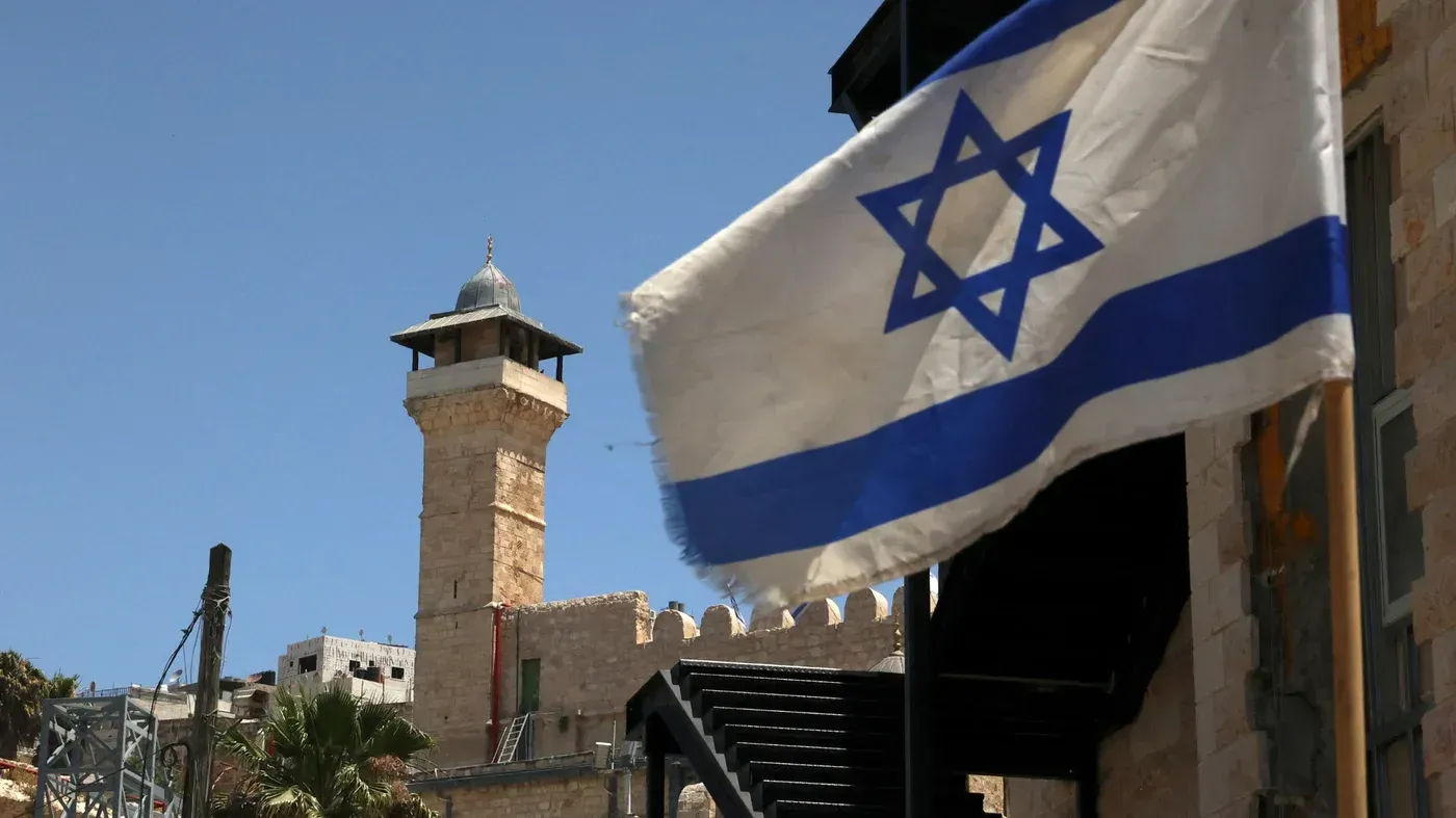 علم إسرائيلي يرفرف أمام منارة الحرم الإبراهيمي في الخليل، رمزًا للصراع على السيطرة بين الفلسطينيين والإسرائيليين.