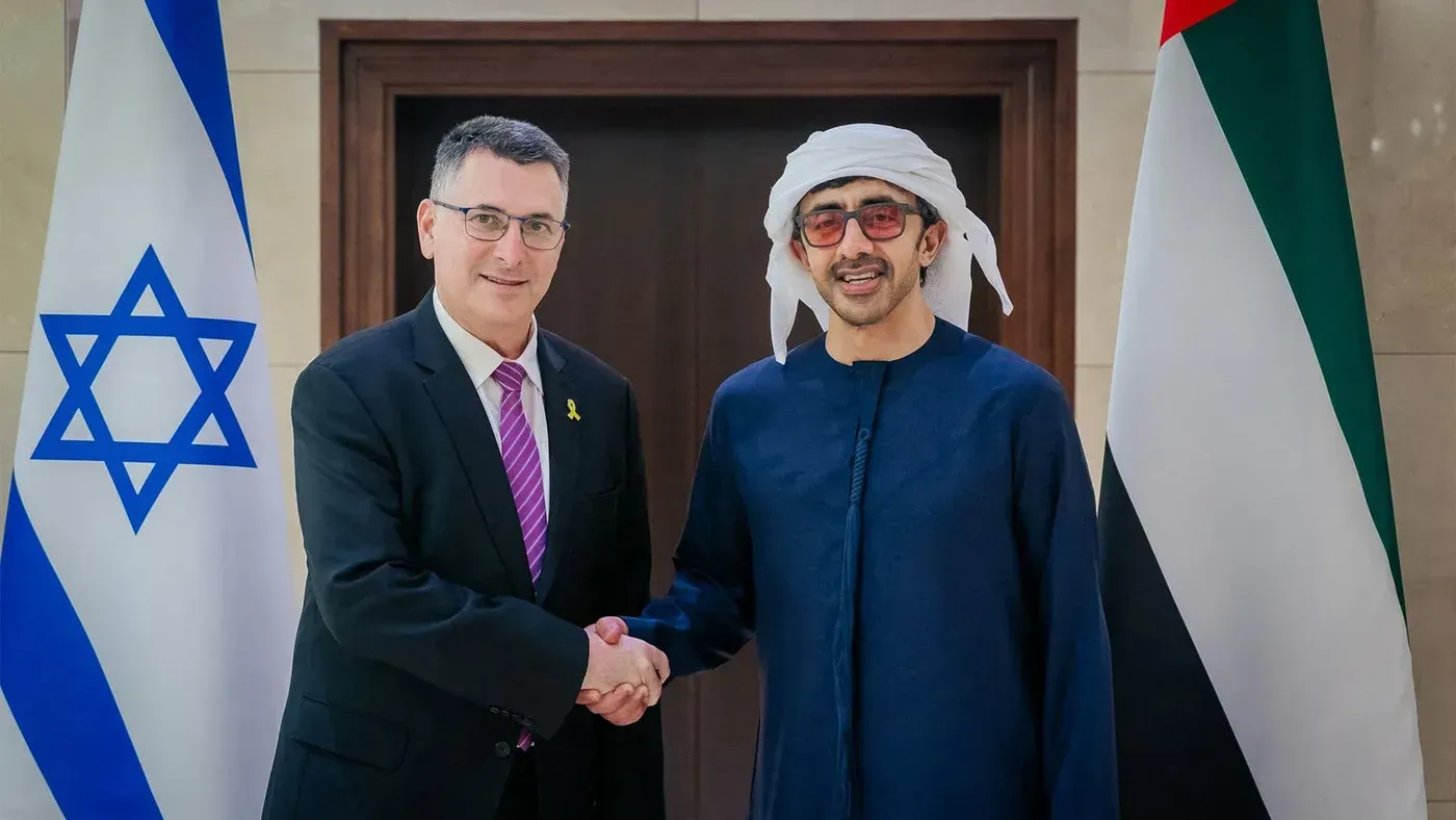 اجتماع بين وزير الخارجية الإسرائيلي ورئيس الإمارات، مع العلميات العسكرية والتعاون الدفاعي في خلفية الصورة.