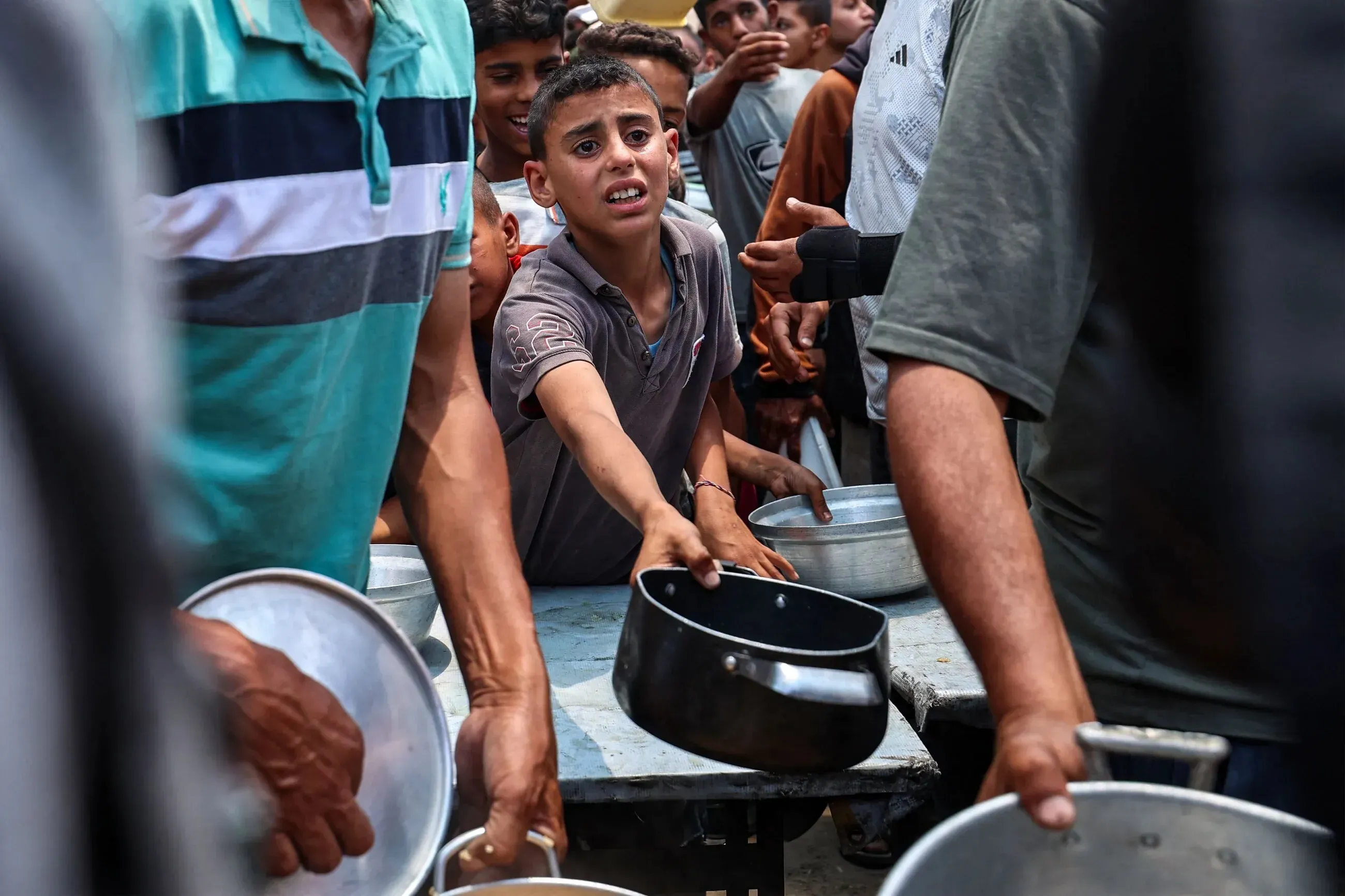 طفل فلسطيني يمد يده للحصول على الطعام وسط حشد من الناس في غزة، معبرًا عن الحاجة الملحة للمساعدات الإنسانية وسط الأزمة المستمرة.