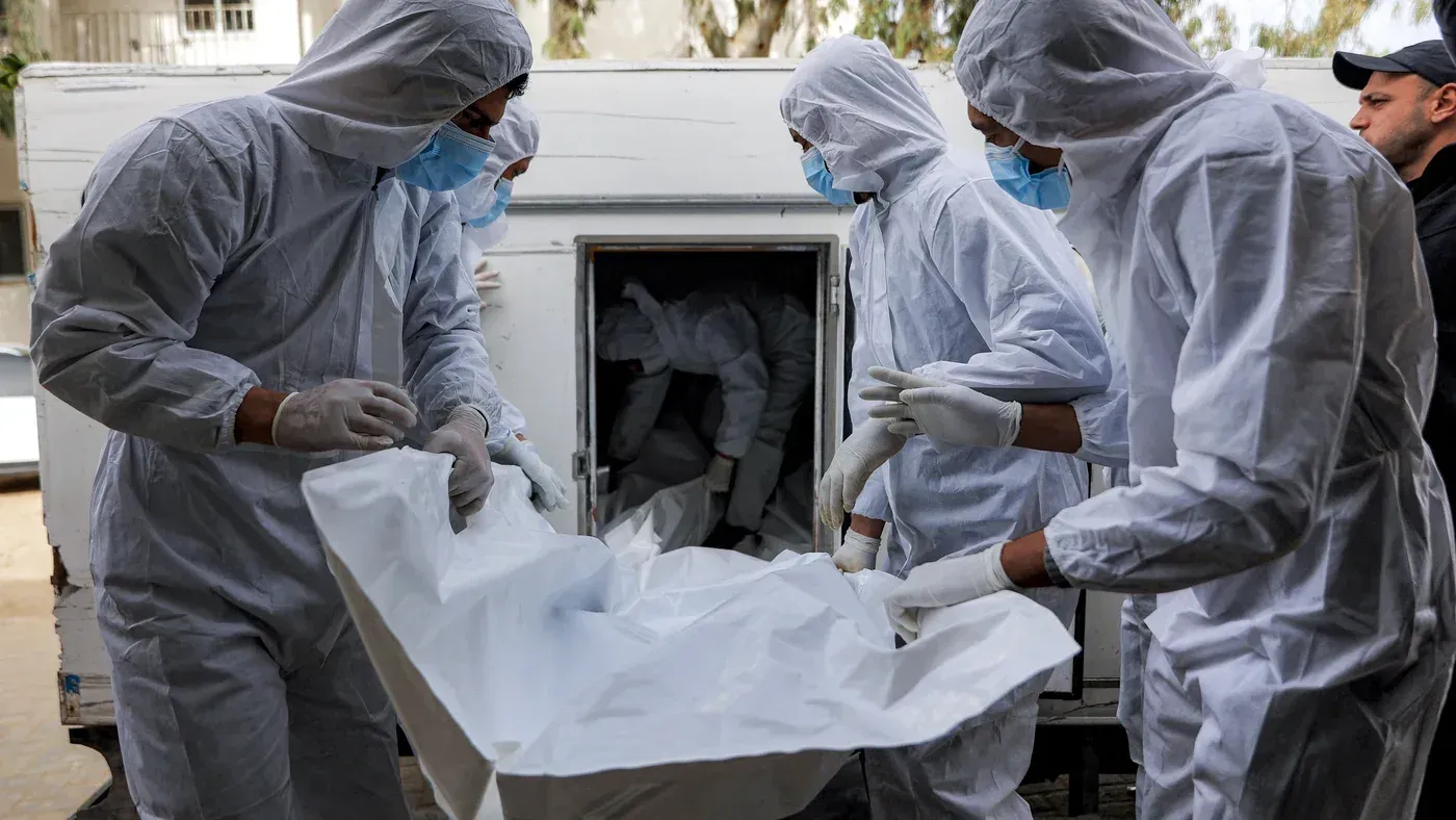 عمال يقومون بنقل جثث فلسطينيين في أكياس بيضاء، يرتدون ملابس واقية وقبعات، في سياق أزمة احتجاز الجثث من قبل السلطات الإسرائيلية.