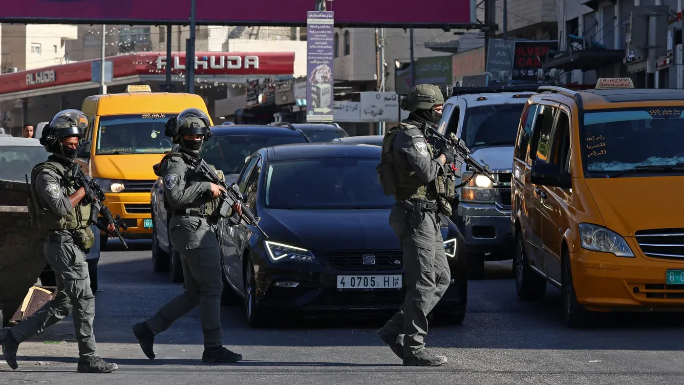 جنود إسرائيليون مسلحون يتقدمون وسط حركة مرور كثيفة في مخيم قلنديا بالقدس الشرقية خلال عملية عسكرية واسعة.