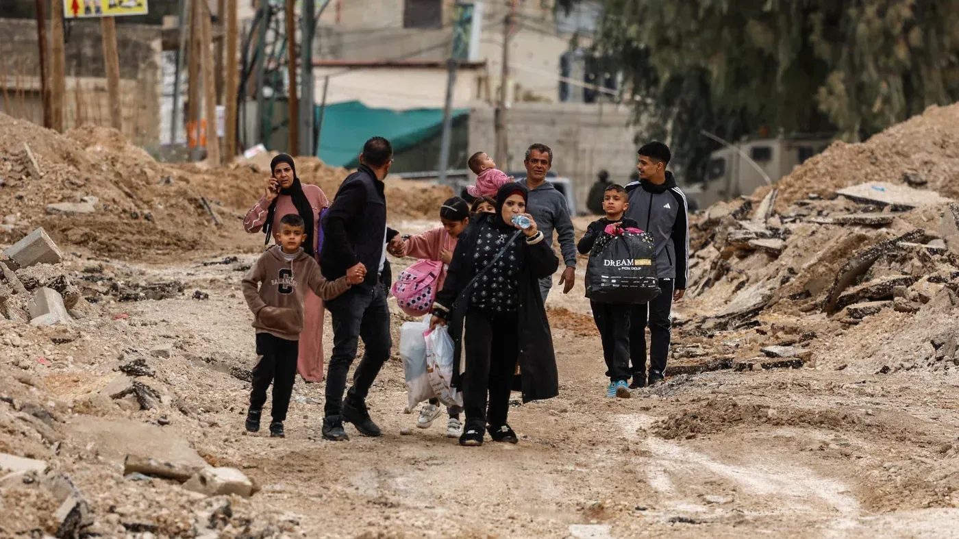 عائلة فلسطينية تسير بين الأنقاض في مخيم جنين بعد الهجوم العسكري الإسرائيلي، تعكس المشهد المؤلم للتدمير والإنسانية في المنطقة.