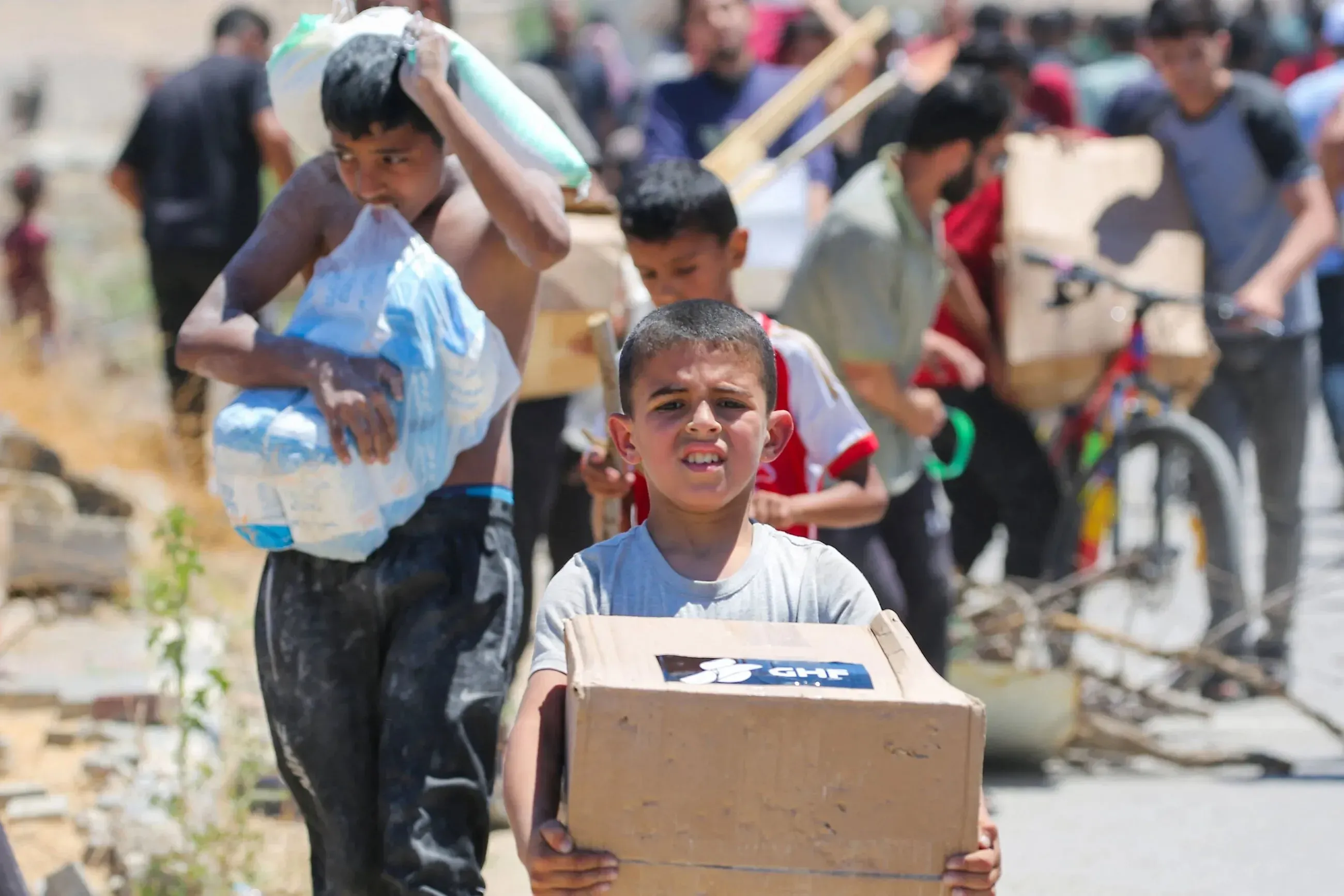 أطفال فلسطينيون يحملون مواد غذائية في رفح، وسط أجواء من الفوضى بعد الهجمات الإسرائيلية على مراكز توزيع المساعدات.