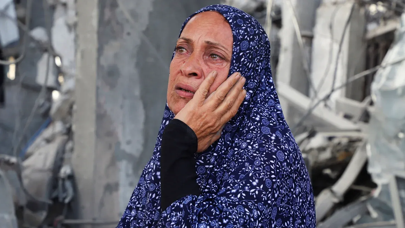 امرأة ترتدي حجابًا مزخرفًا، تعبر عن الحزن والقلق في وسط أنقاض، تعكس تأثير القيود الإسرائيلية على المساعدات الإنسانية في غزة.