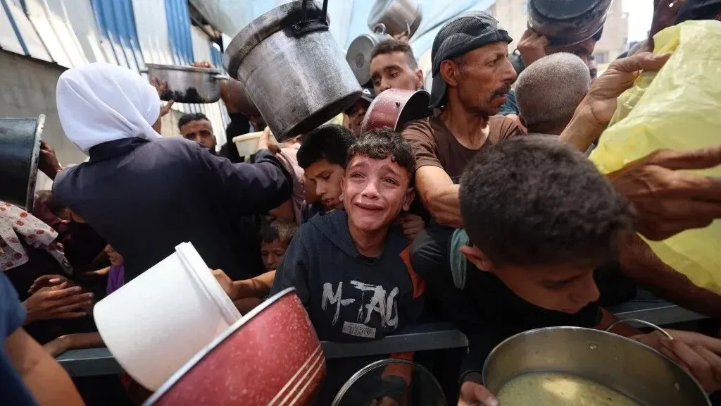 طفل يبكي وسط حشد من الأشخاص الذين يتزاحمون للحصول على الطعام في غزة، مما يعكس أزمة إنسانية حادة وتحديات توزيع المساعدات.