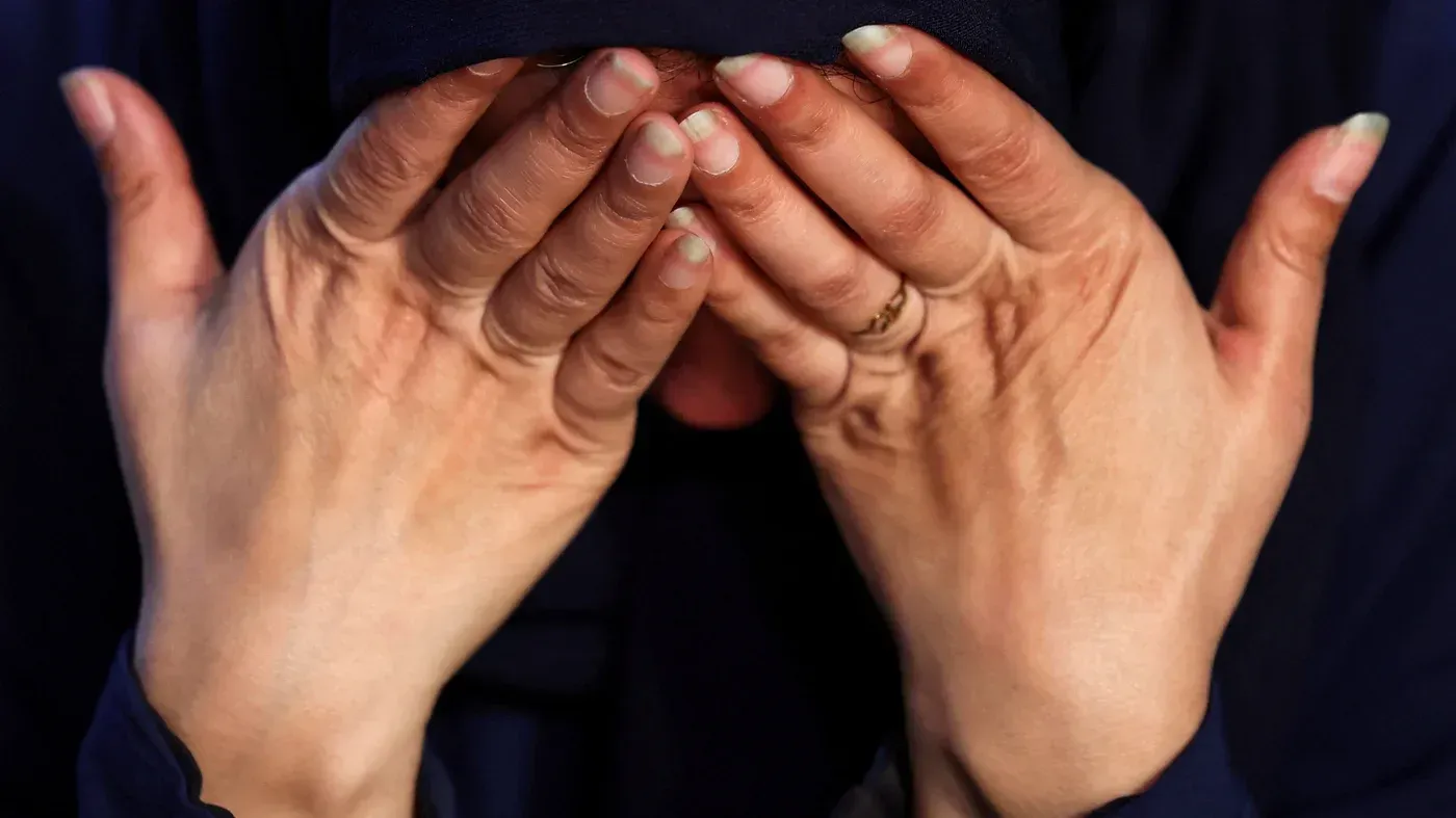 امرأة فلسطينية تغطي وجهها بيديها تعبيرًا عن الألم والقلق، في سياق معاناة العائدين إلى غزة بعد الاستجواب من القوات الإسرائيلية.