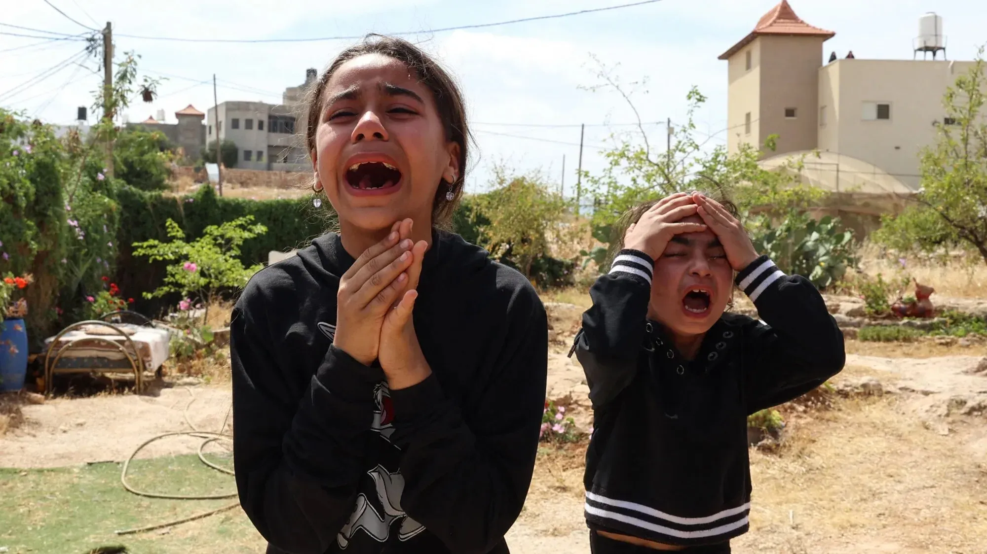 طفلتان فلسطينيتان تبكيان في حديقة، تعبران عن الحزن والخوف بعد الأحداث العنيفة في الضفة الغربية، في ظل الأوضاع المتوترة.