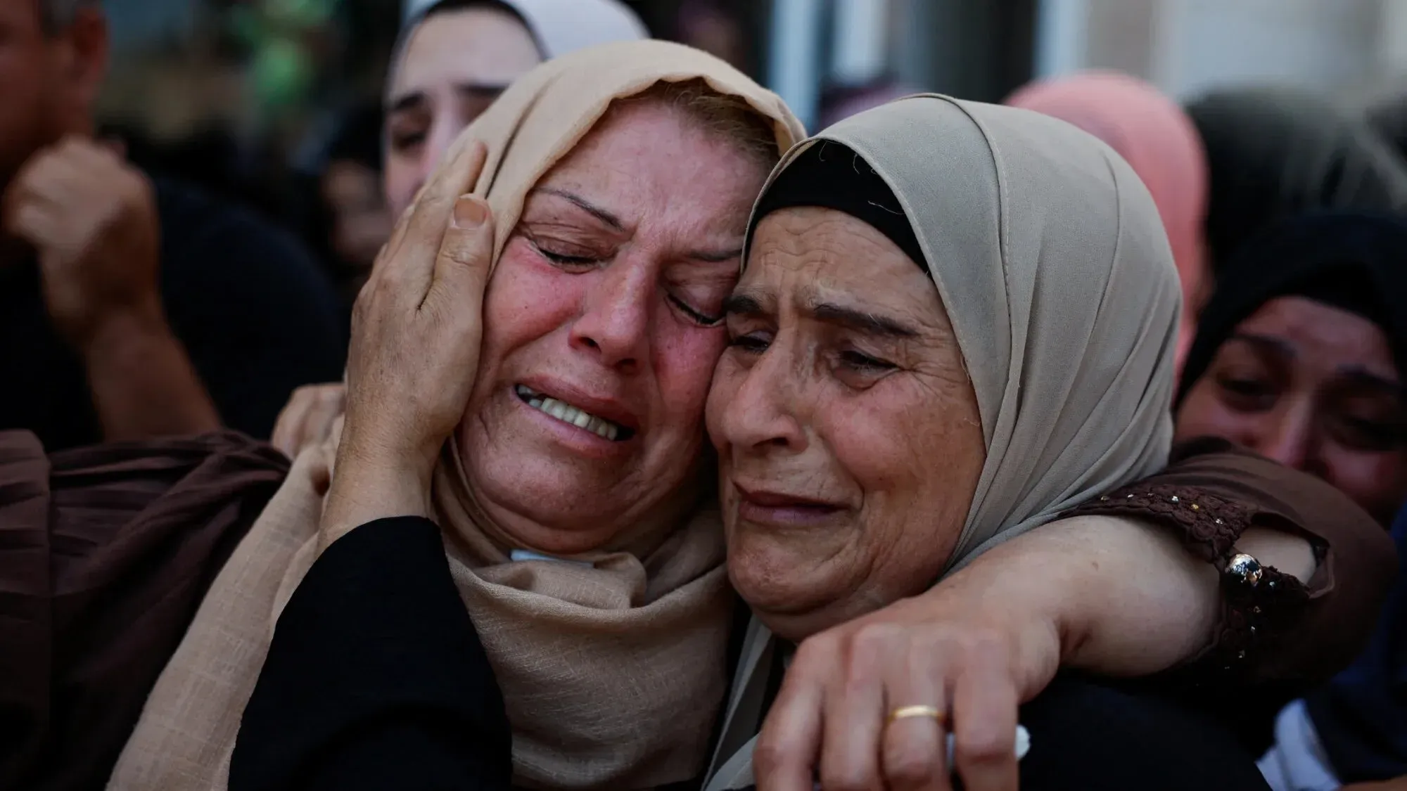 امرأتان فلسطينيتان تبكيان بحرقة أثناء تشييع ضحايا الهجوم الإسرائيلي في كفر مالك، مع تعبيرات حزينة تعكس الألم والغضب.