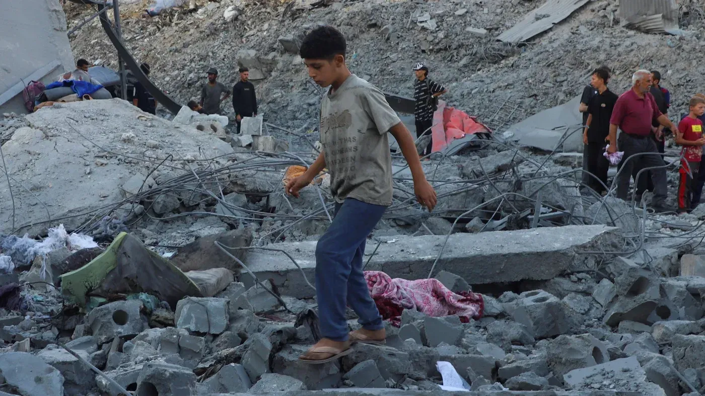 طفل يسير بين الأنقاض في حي الدرج بغزة، حيث تضررت المنطقة بشدة جراء الغارات الجوية، مع وجود أشخاص آخرين في الخلفية.