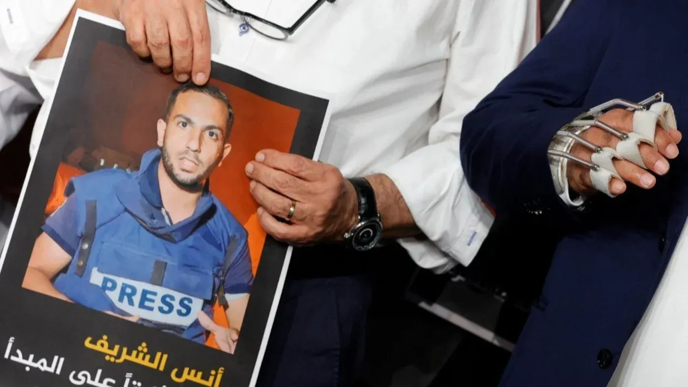 صورة تظهر شخصين يحملان لافتة تتضمن صورة الصحفي أنس الشريف الذي قُتل في غزة، مع تعبير عن التضامن مع حرية الصحافة.