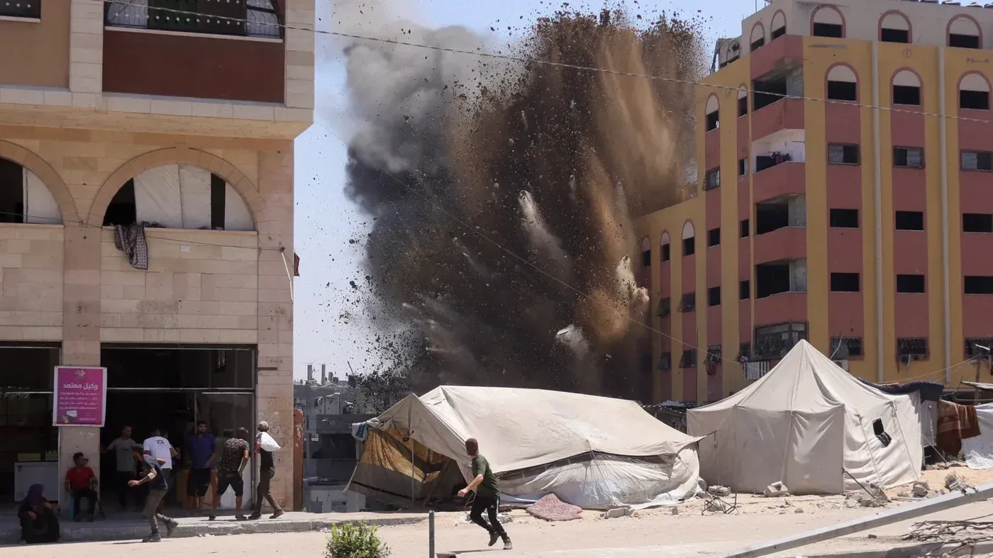 انفجار قوي في منطقة سكنية، مع تصاعد الغبار والدخان، بينما يهرع الناس للابتعاد عن الموقع. tents في المقدمة.