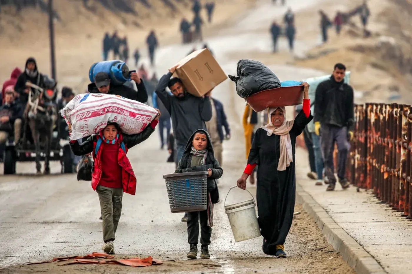 أطفال ونساء فلسطينيون يحملون أمتعتهم وسط أجواء من التوتر، يعكسون معاناة النزوح من غزة في ظل الأوضاع الراهنة.