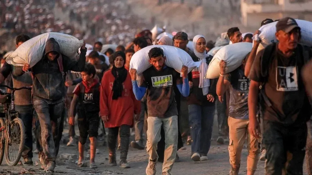 أشخاص في غزة يحملون أعباء ثقيلة من المساعدات الإنسانية، مع تزايد الحاجة إلى الإغاثة بسبب الأوضاع الصعبة.