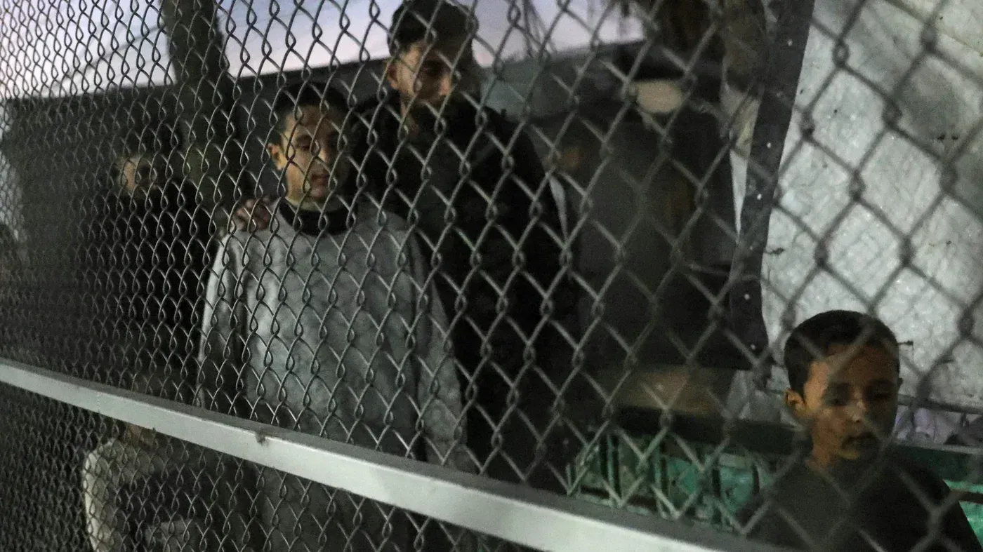 أطفال فلسطينيون يقفون خلف سياج معدني في مركز احتجاز، يعكس الأوضاع الصعبة التي يواجهها الأسرى في ظل التوترات الحالية.
