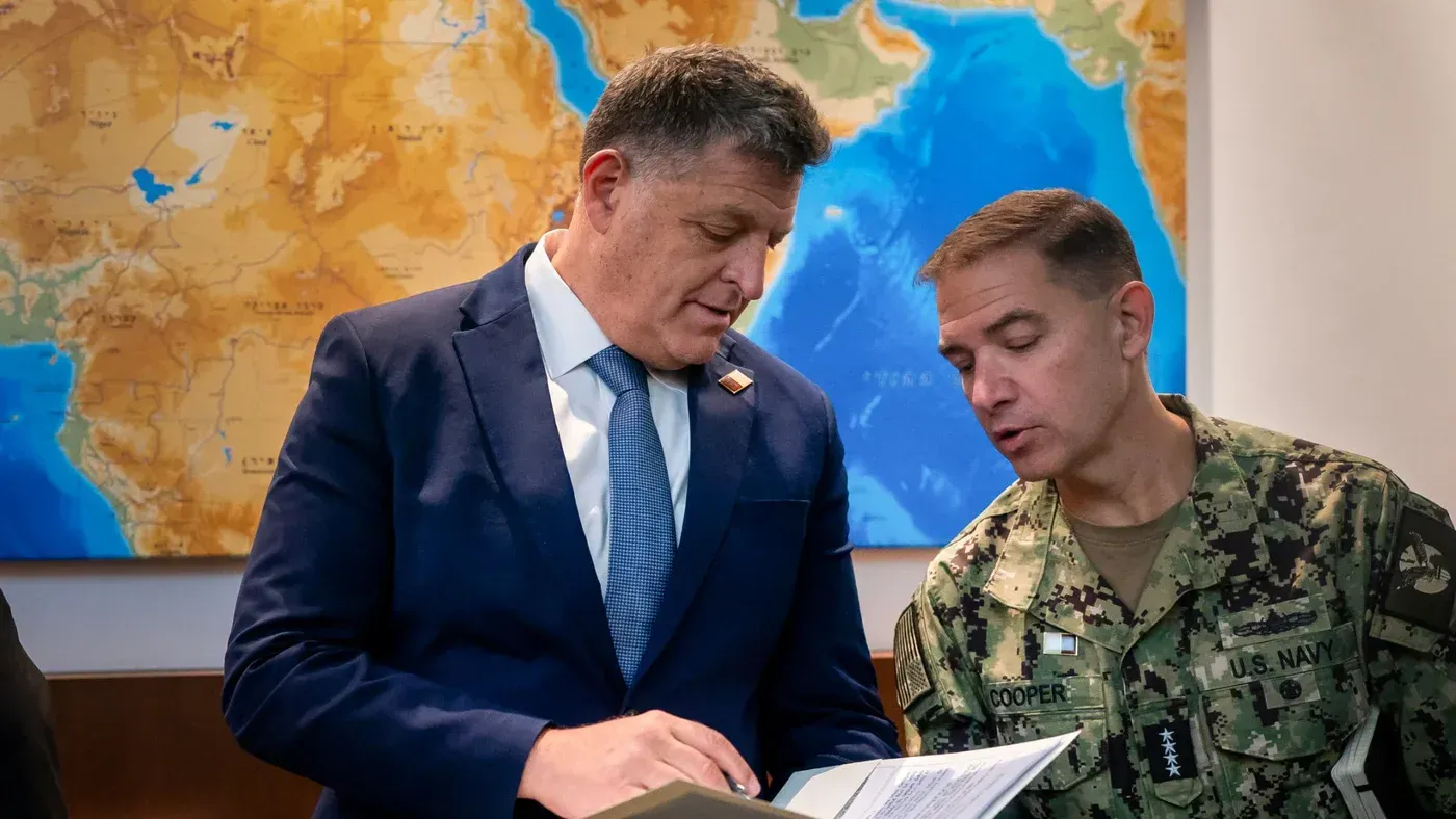 اجتماع بين مسؤولين عسكريين، مع خريطة خلفية توضح منطقة الشرق الأوسط، حيث يناقشون التعاون اللوجستي والاستخباراتي لدعم الجيش الأمريكي.